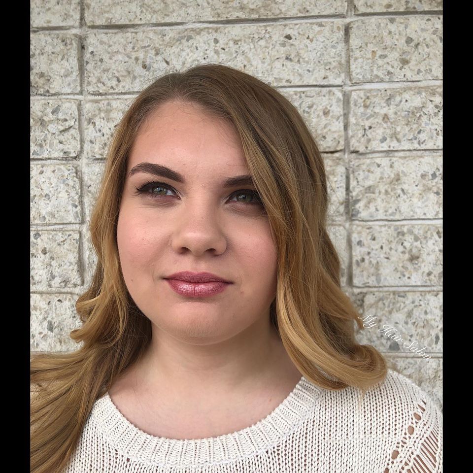 A woman in a white sweater is standing in front of a brick wall.
