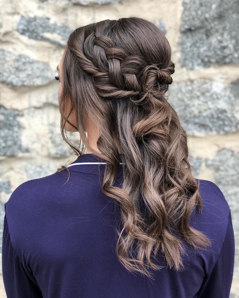 The woman is wearing a purple shirt and has her hair in a half up half down braid.
