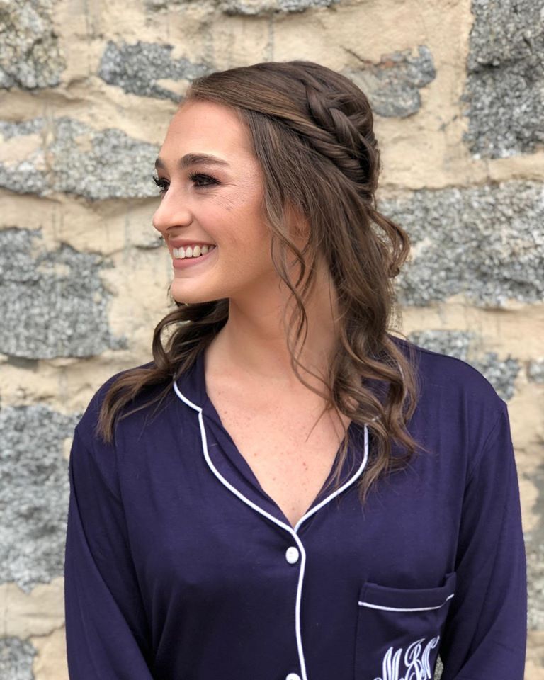 A woman wearing a purple shirt with a monogram on the pocket is smiling.