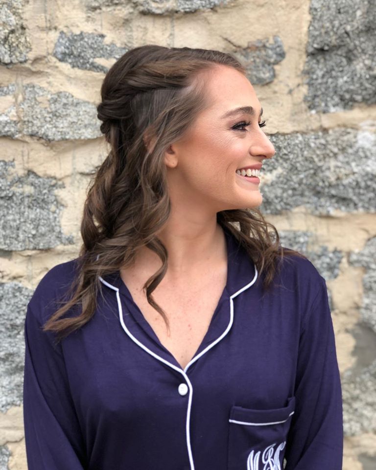 A woman in a purple shirt with a monogram on the pocket is smiling.