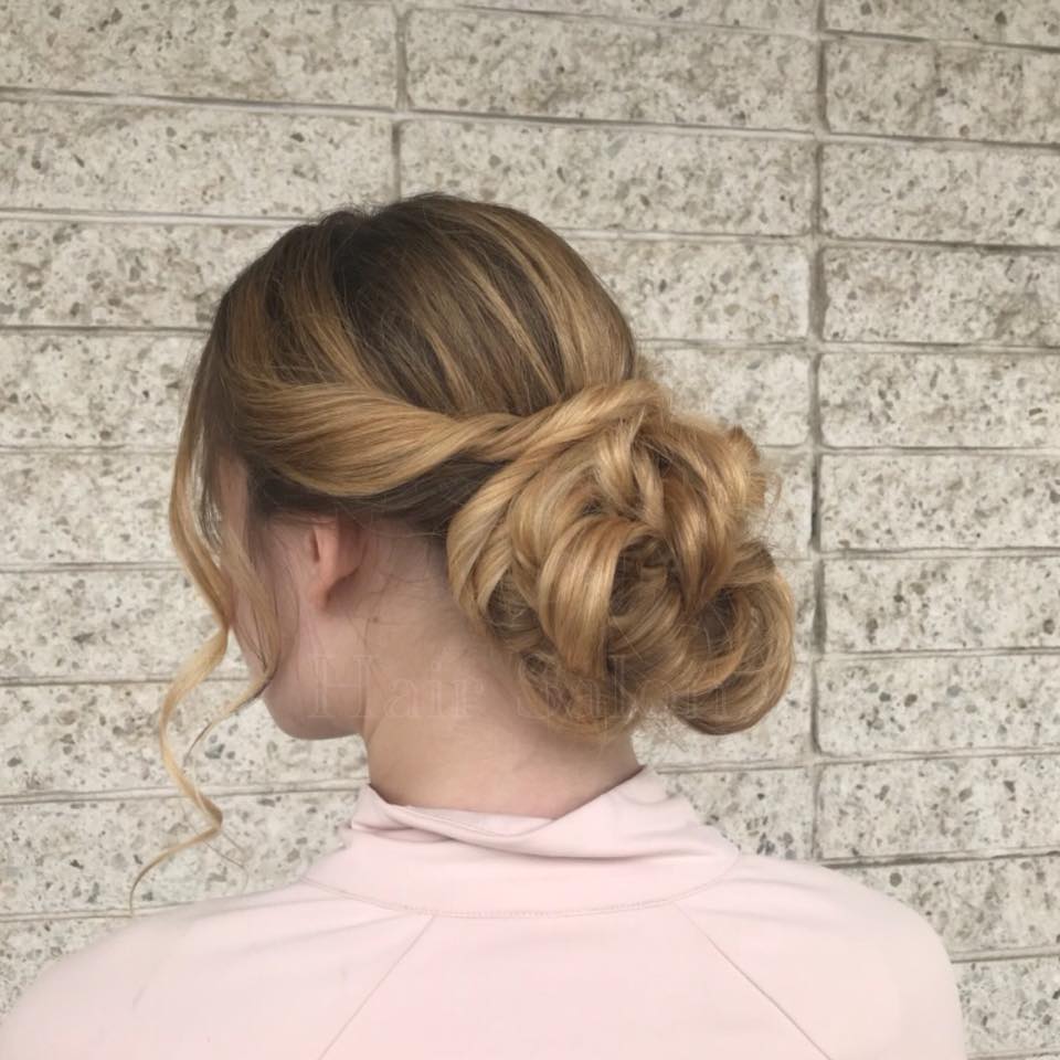 A woman with her hair in a bun is standing in front of a brick wall.