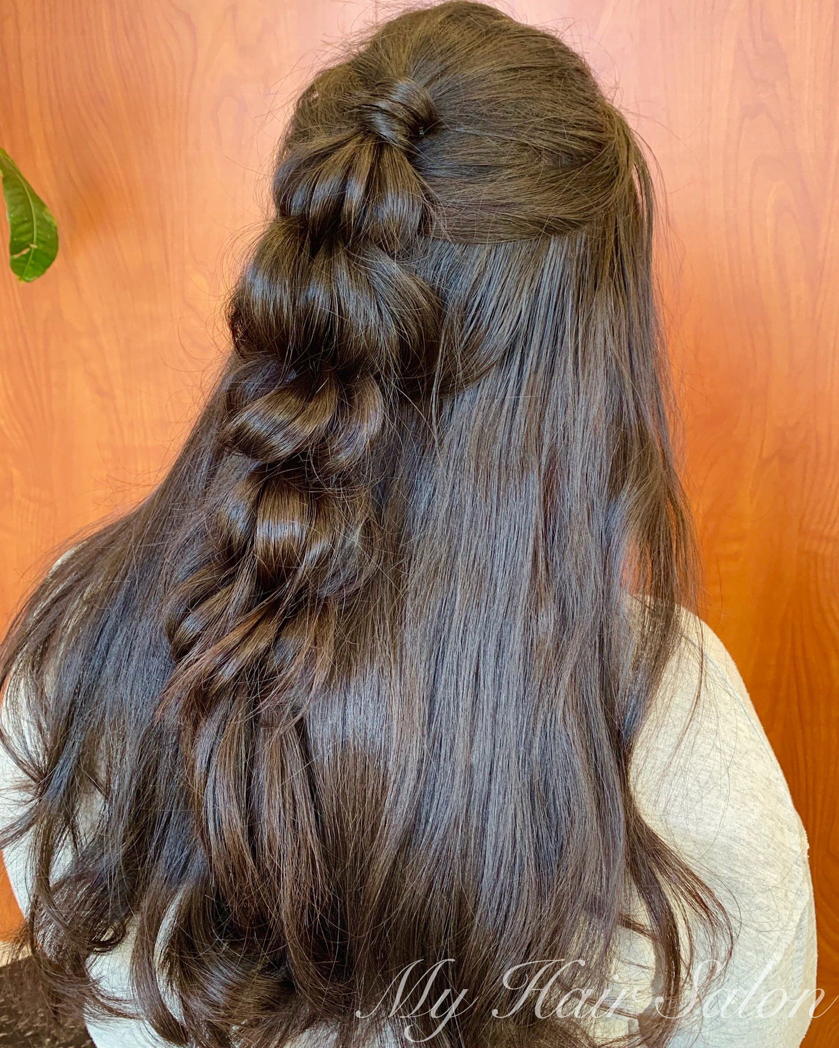 A woman with long hair is wearing a braided half up half down hairstyle.