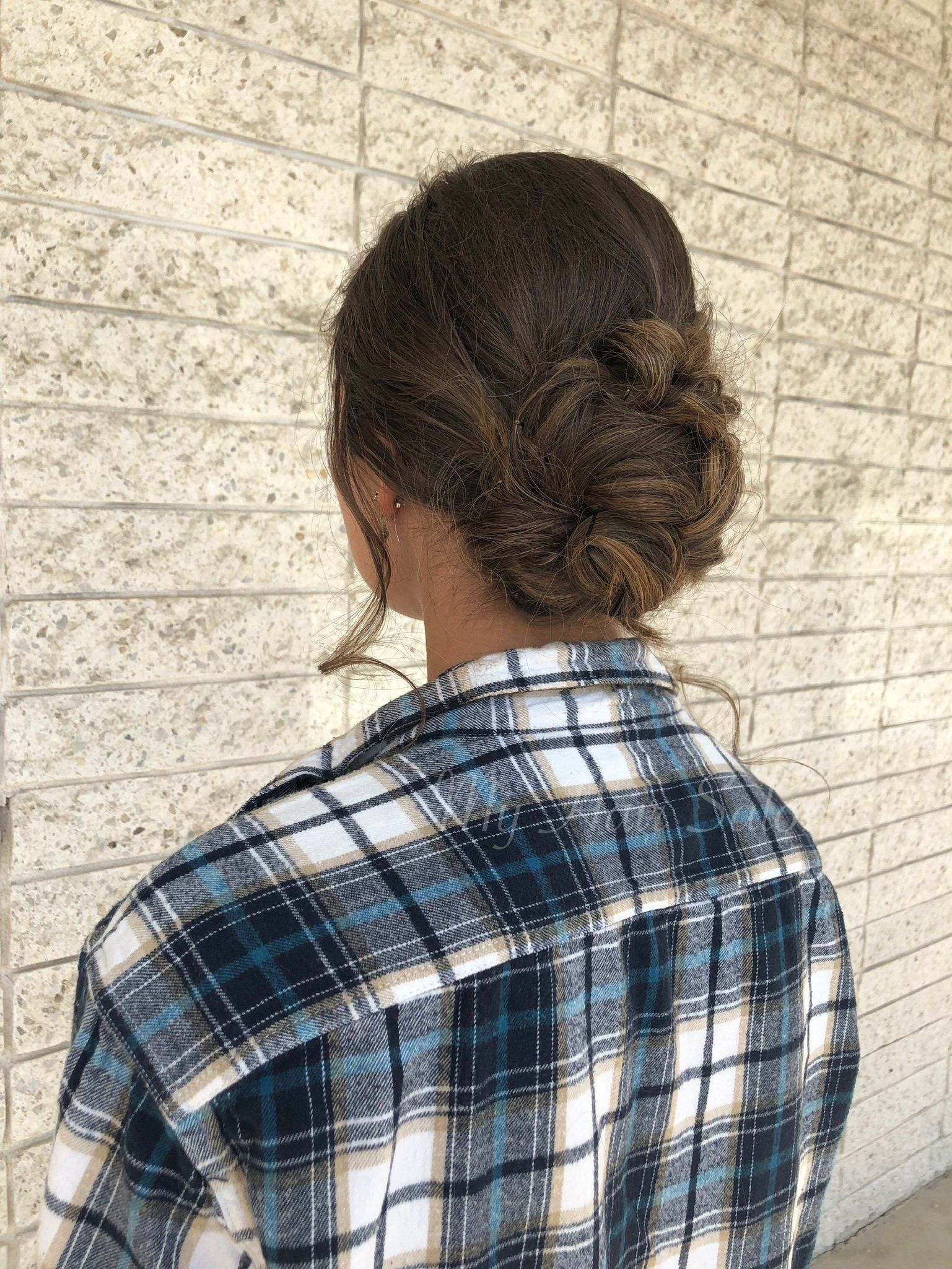A woman wearing a plaid shirt and a bun is standing in front of a brick wall.