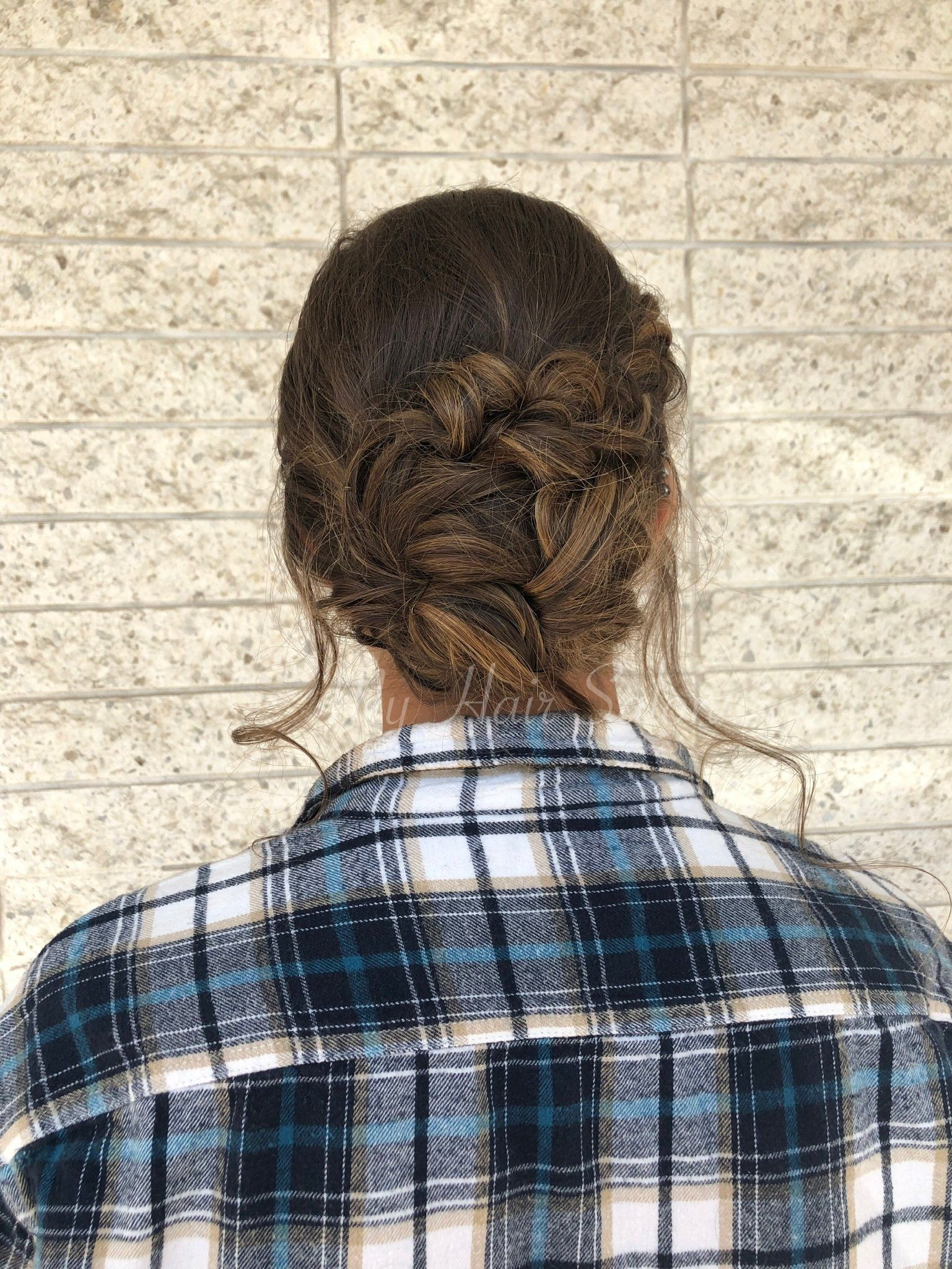The back of a person wearing a plaid shirt and a braided bun.