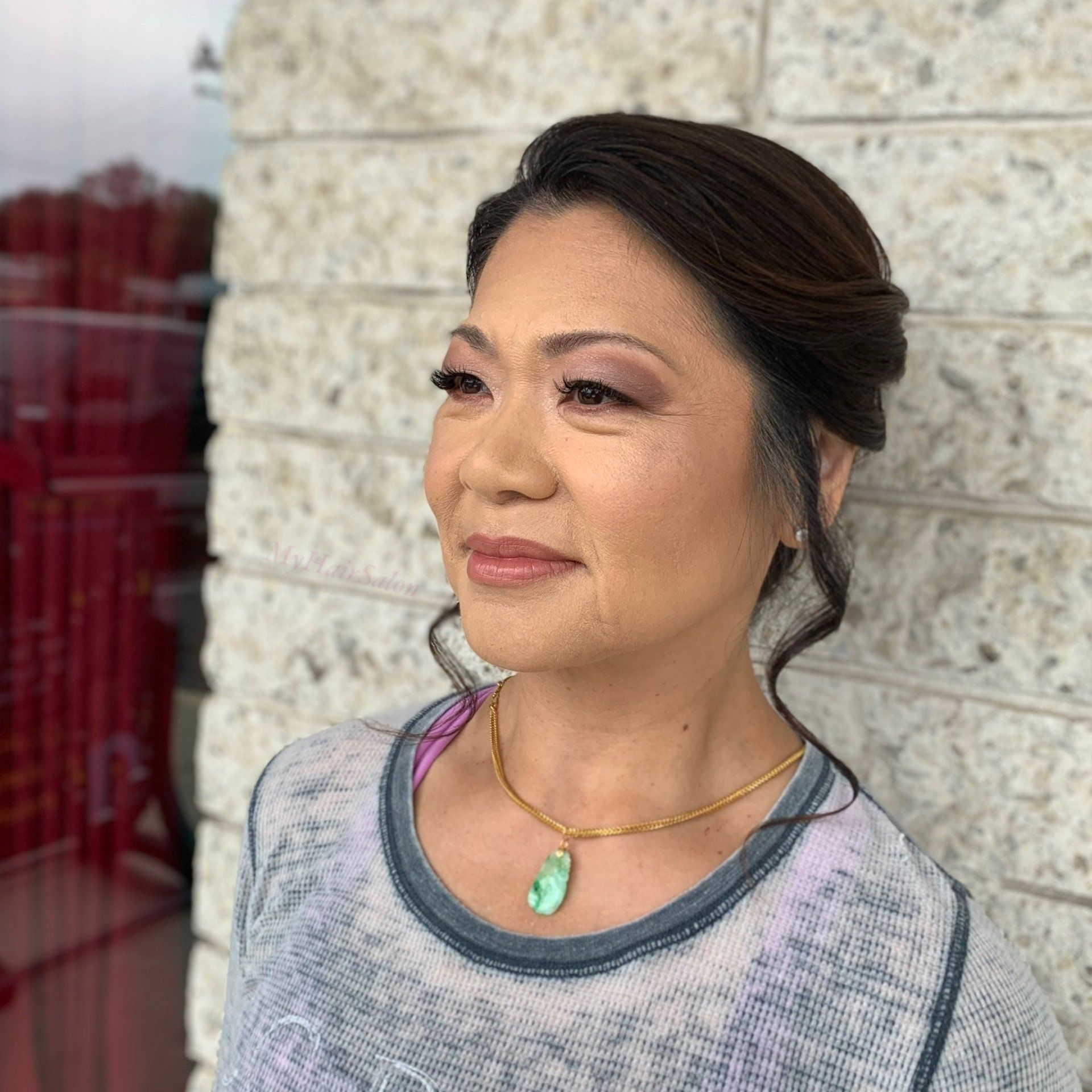 A woman wearing a necklace is standing in front of a brick wall.