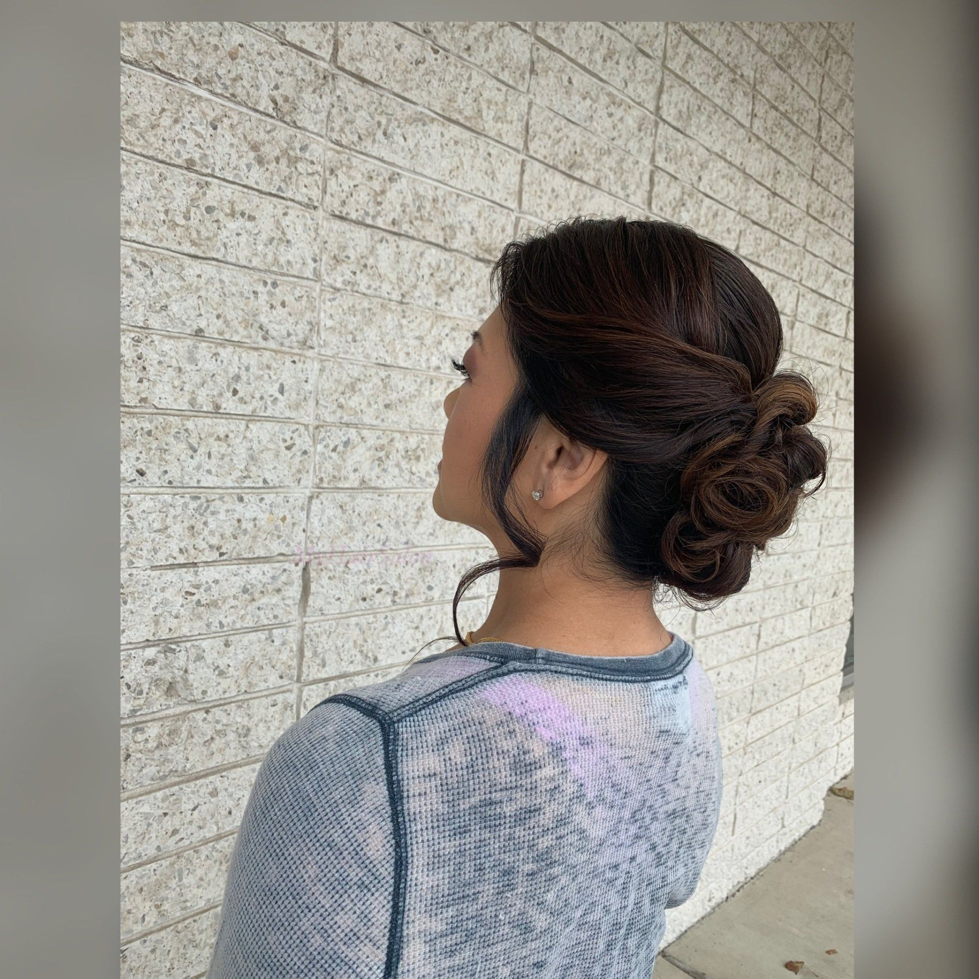 A woman with her hair in a bun is standing in front of a brick wall.