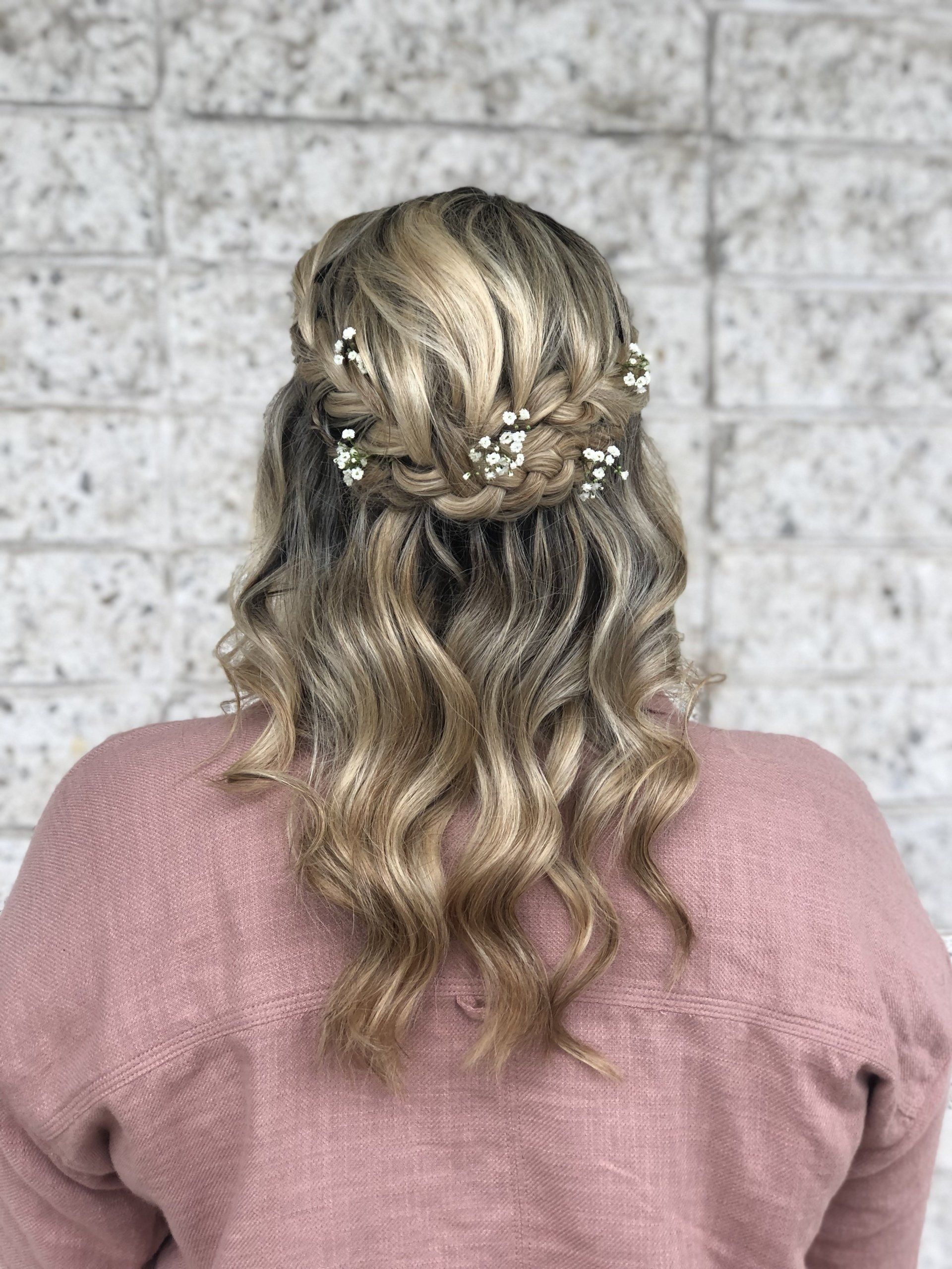 The back of a woman wearing a pink sweater and a half up half down hairstyle.