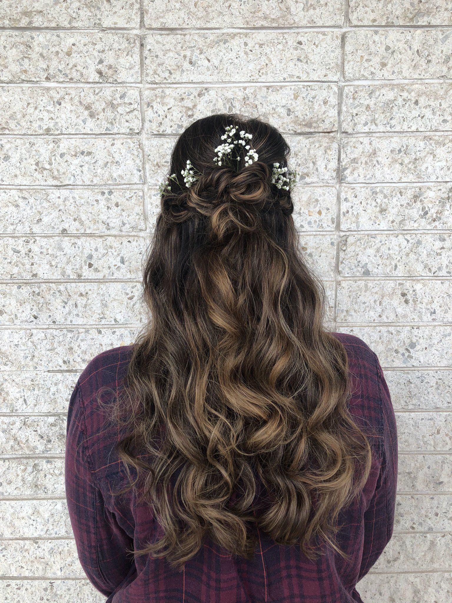 The back of a woman wearing a half up half down hairstyle with flowers in her hair.