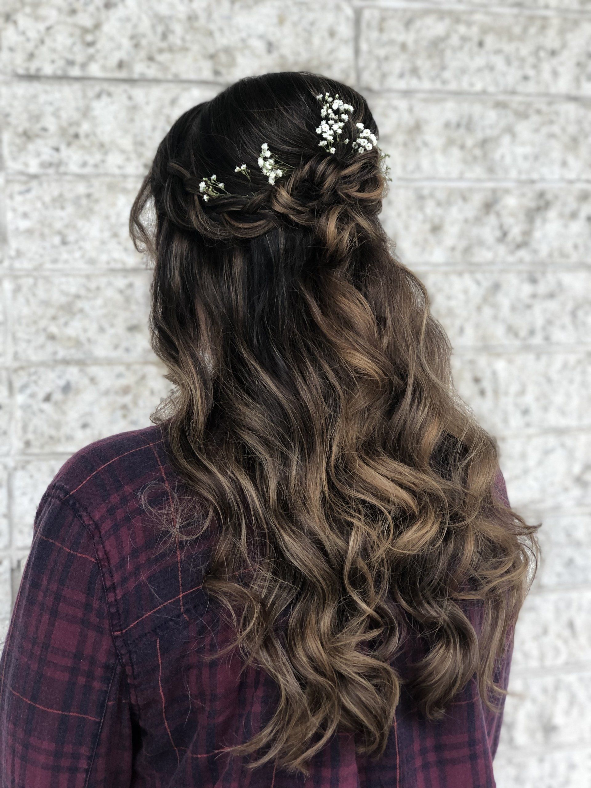 A woman wearing a plaid shirt and a half up half down hairstyle with flowers in her hair.