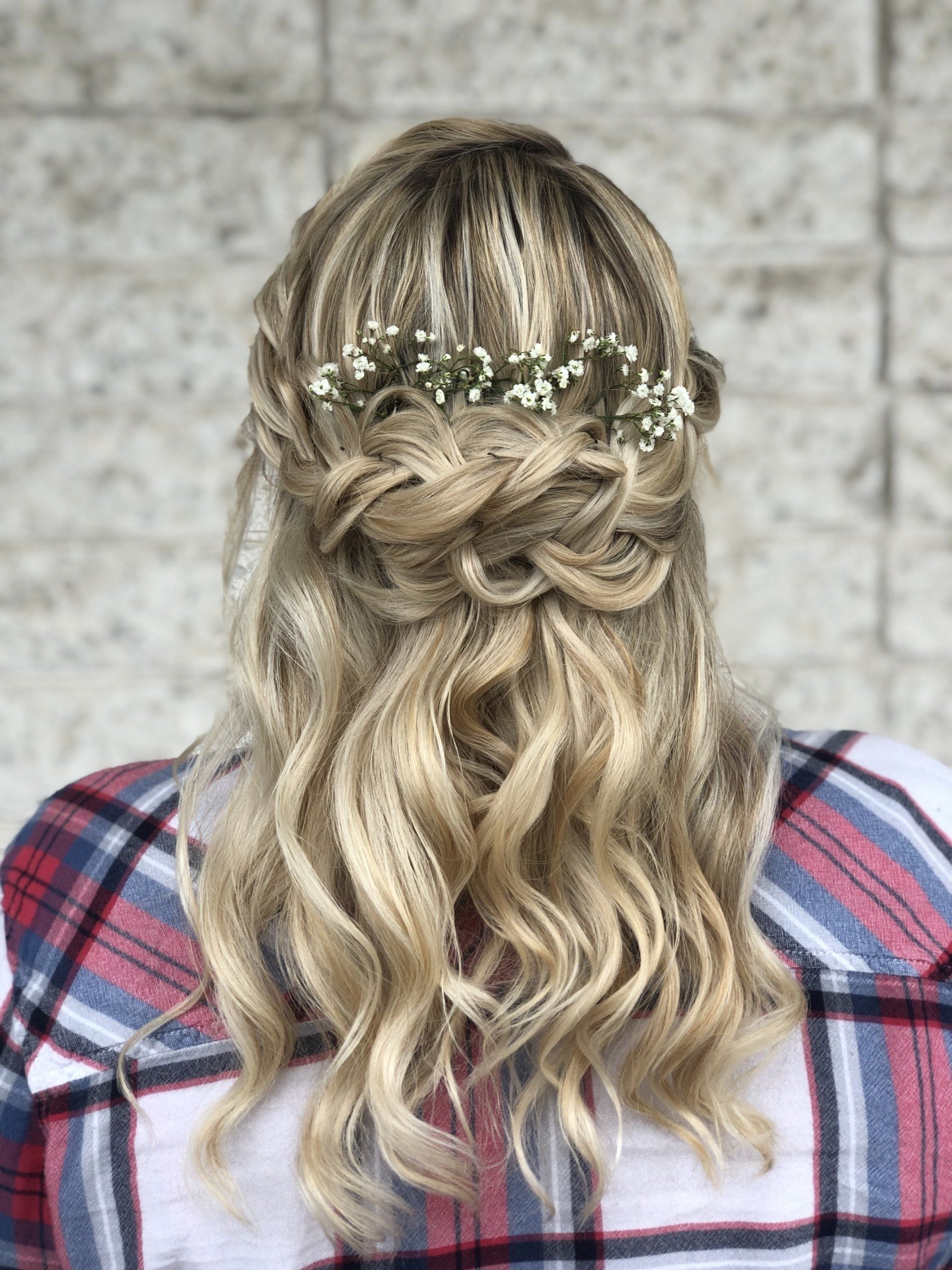 A woman wearing a plaid shirt and a half up half down hairstyle with baby 's breath in her hair.