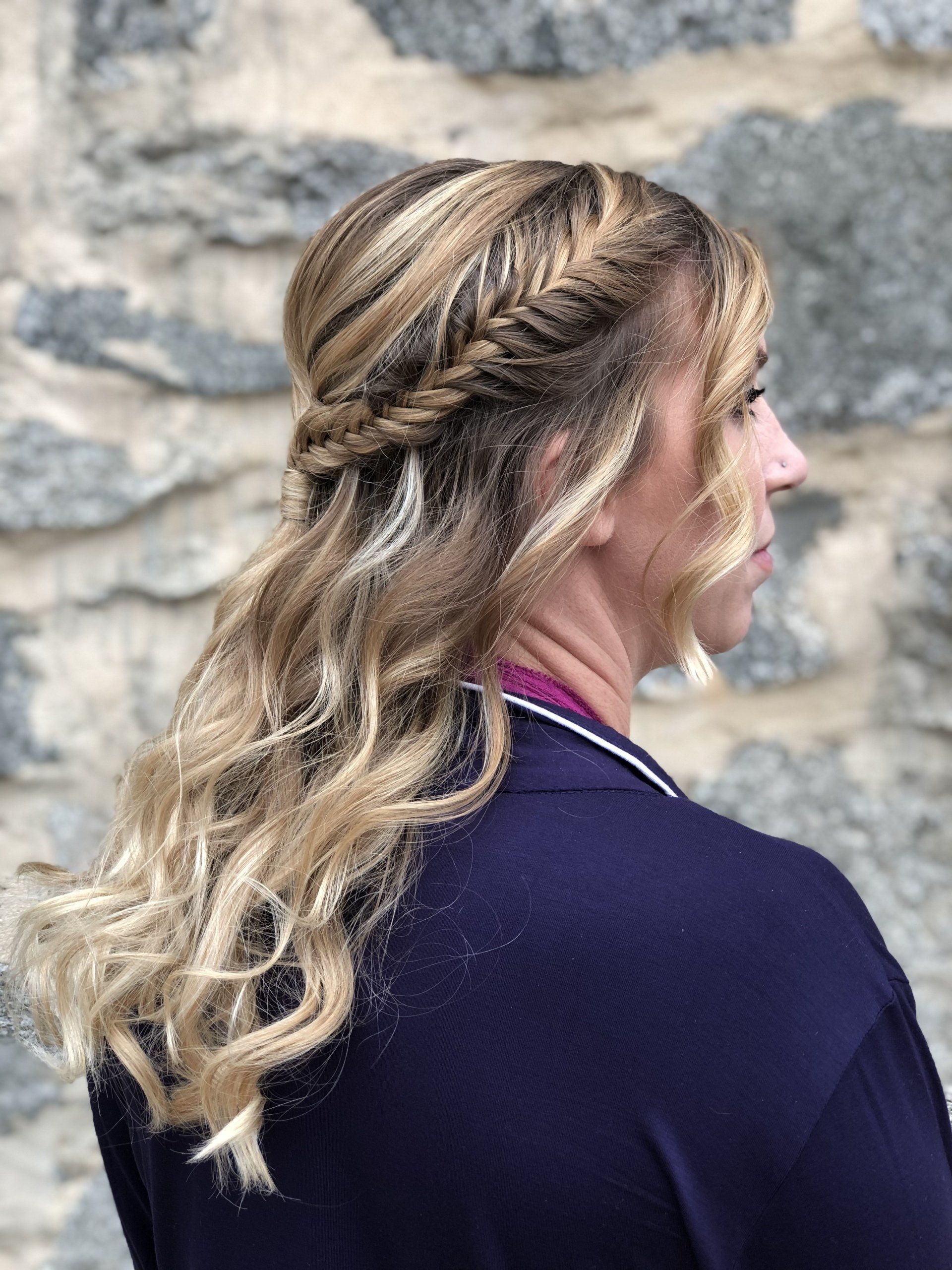 A woman with long blonde hair is wearing a braided half up half down hairstyle.