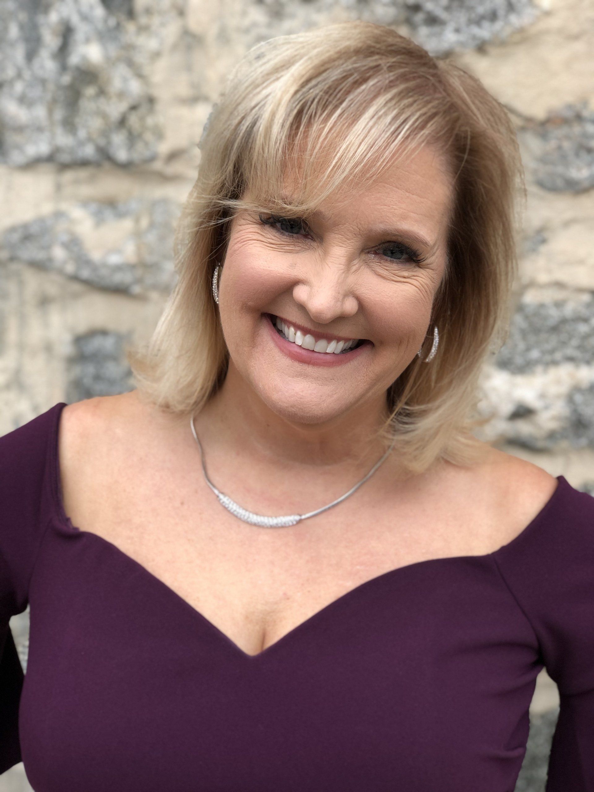 A woman in a purple top and necklace is smiling for the camera.