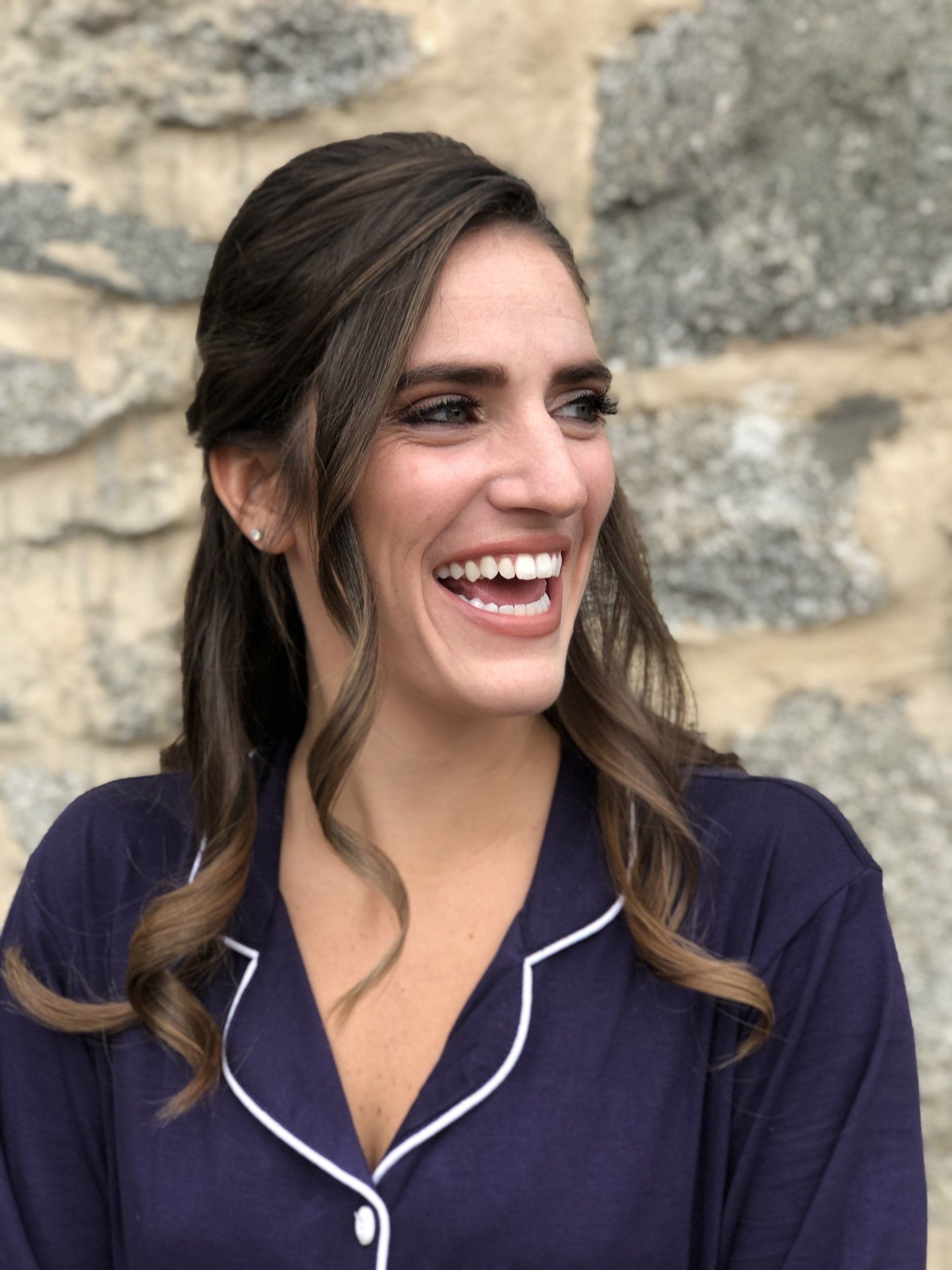 A woman in a blue shirt is smiling in front of a stone wall