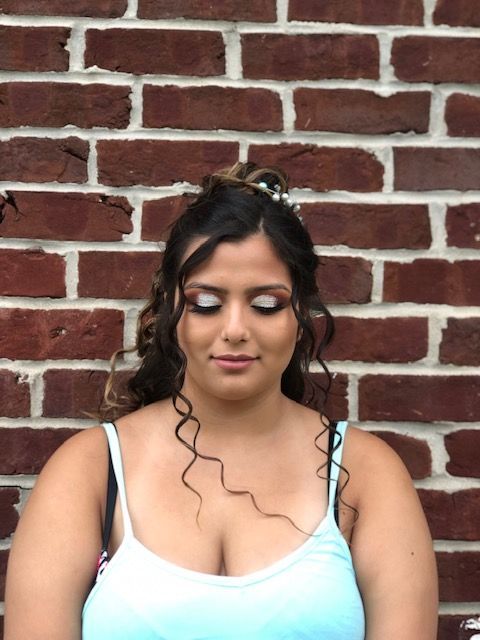 A woman in a blue tank top stands in front of a brick wall