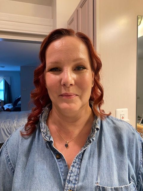 A woman with red hair is wearing a blue shirt and a necklace.