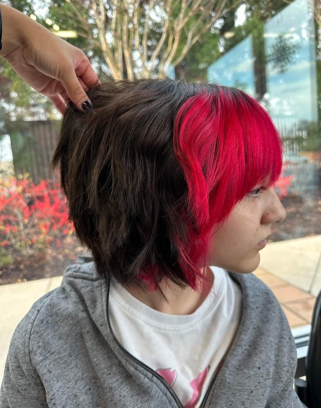 A person with red and black hair is getting their hair cut.