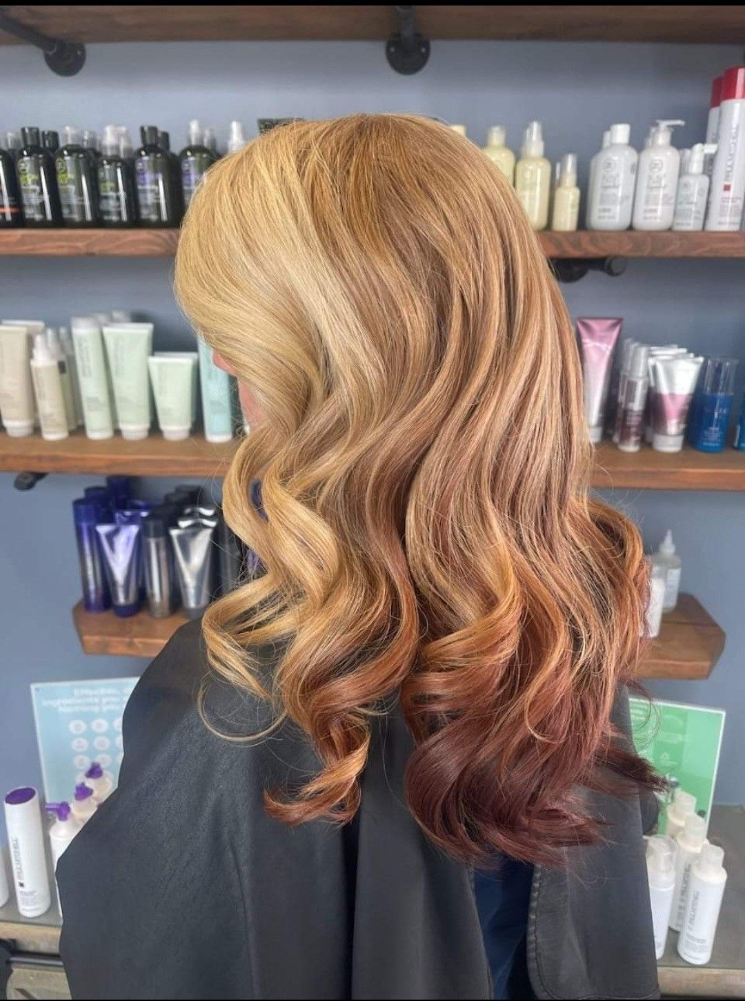 A woman with blonde and red hair is standing in front of a shelf of hair products.