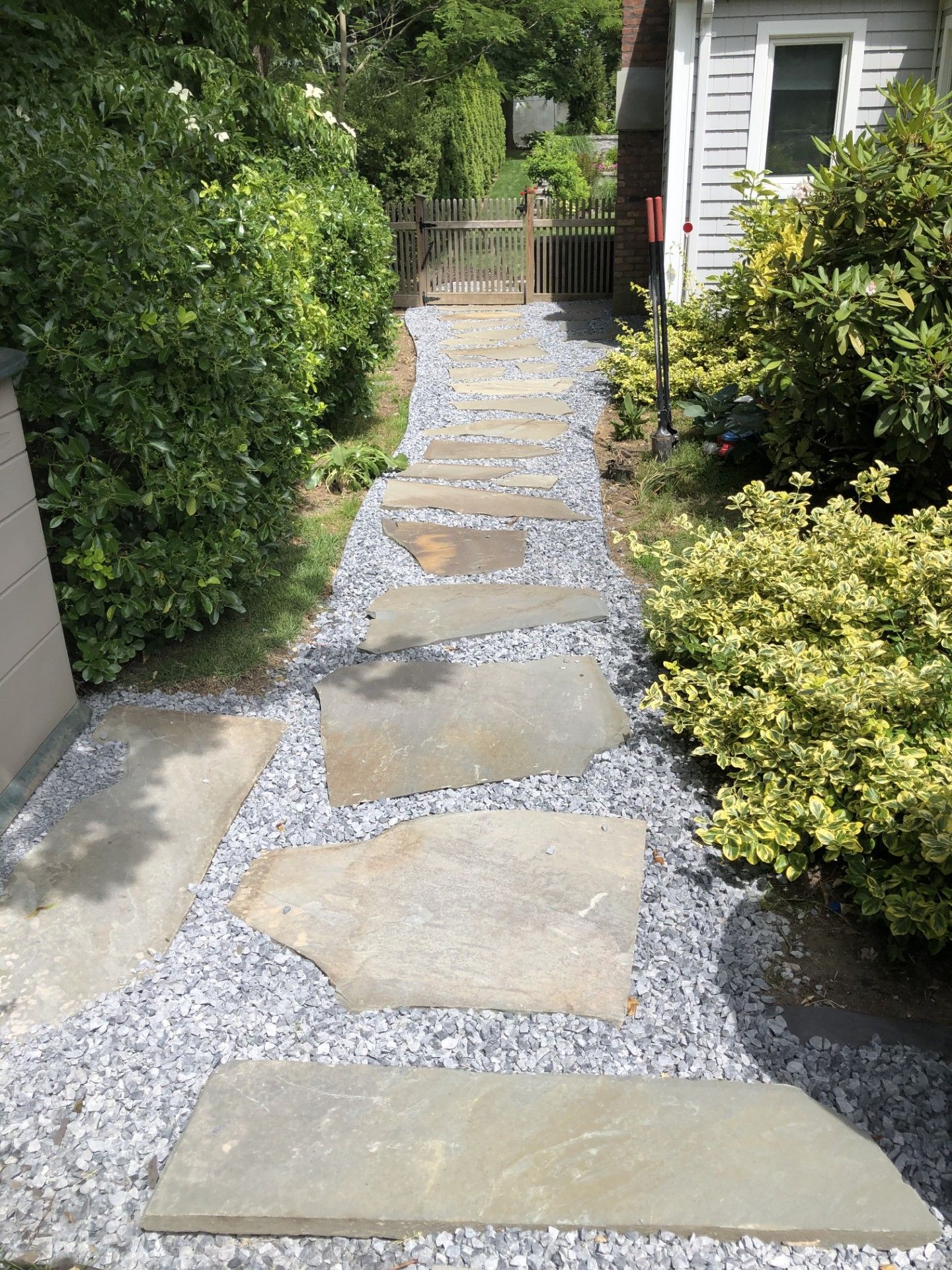 A stone walkway leading to a house surrounded by bushes