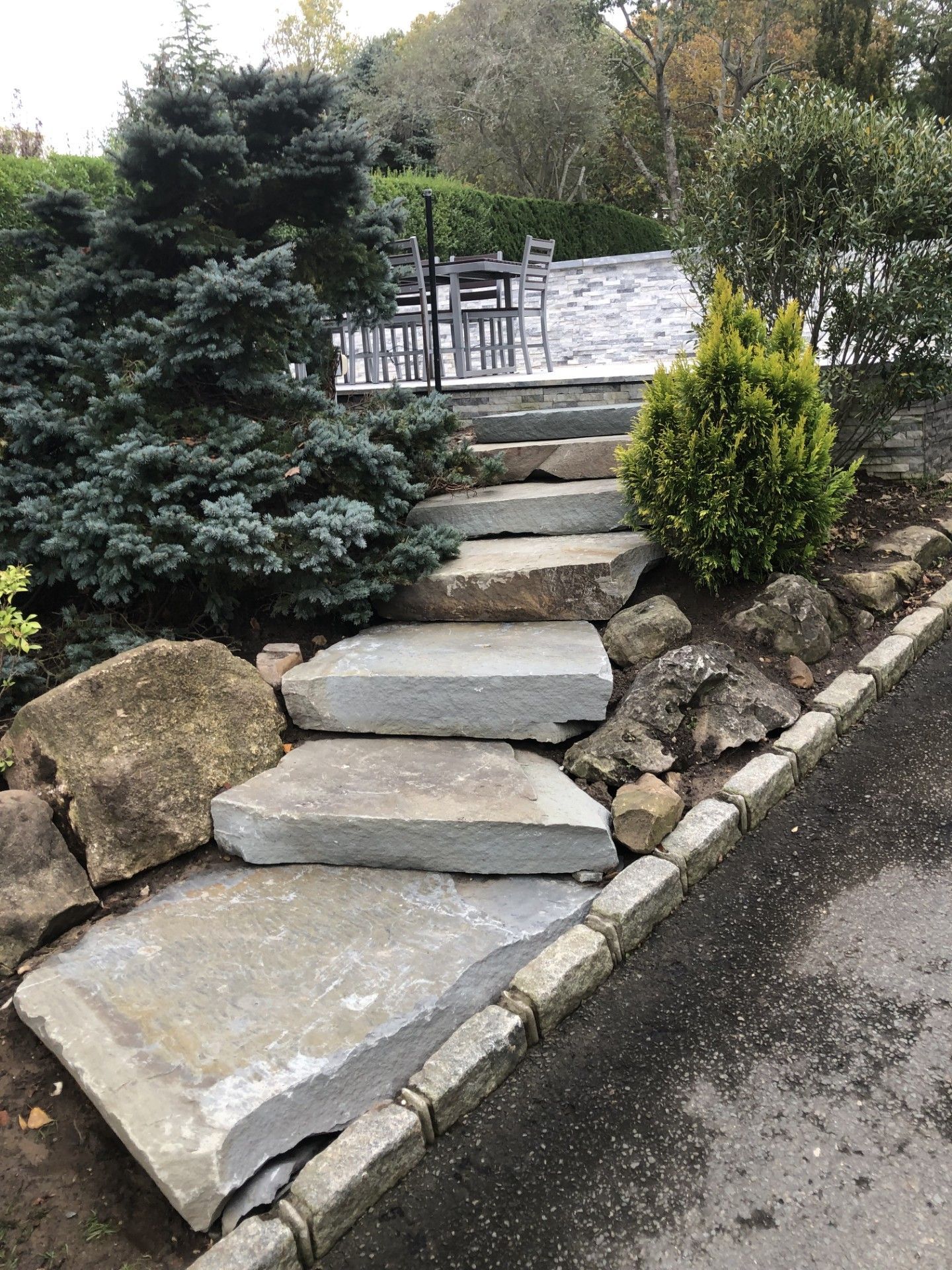 A stone walkway leading to a patio with a table and chairs.