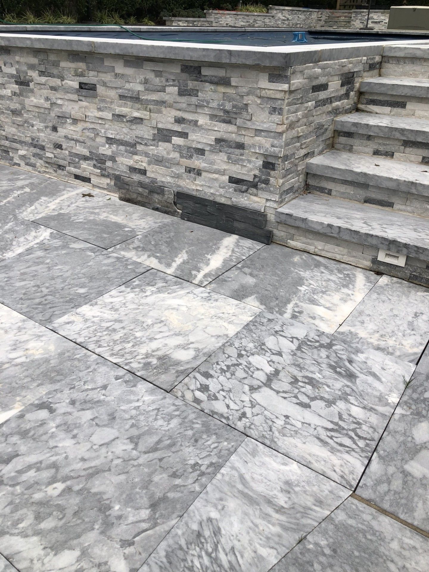 A patio with a stone wall and stairs next to a pool.