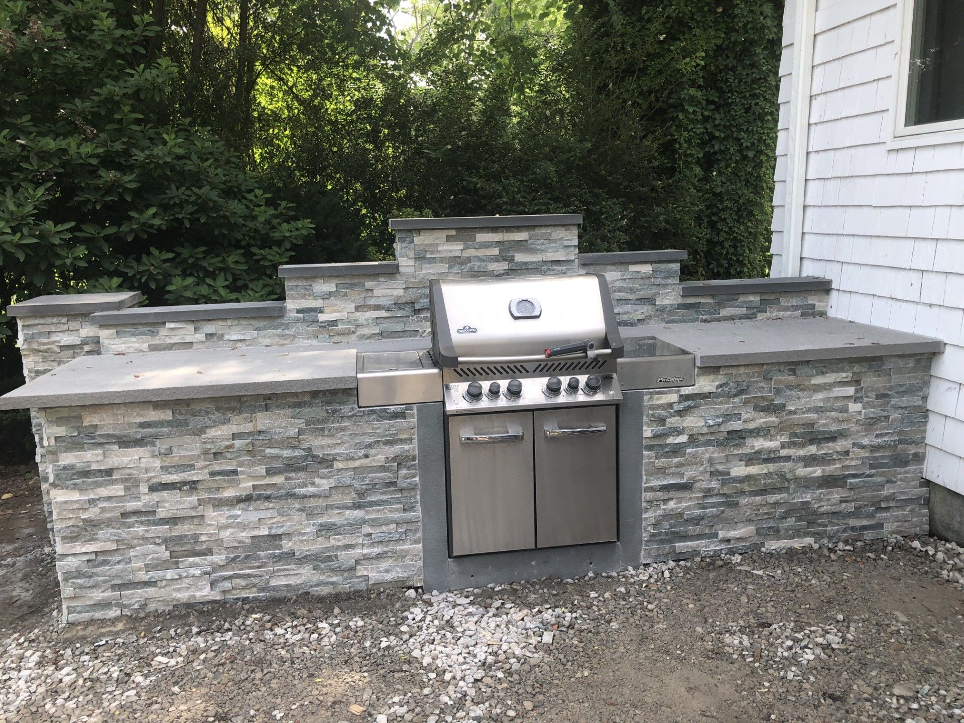 A grill is built into a stone wall next to a house.