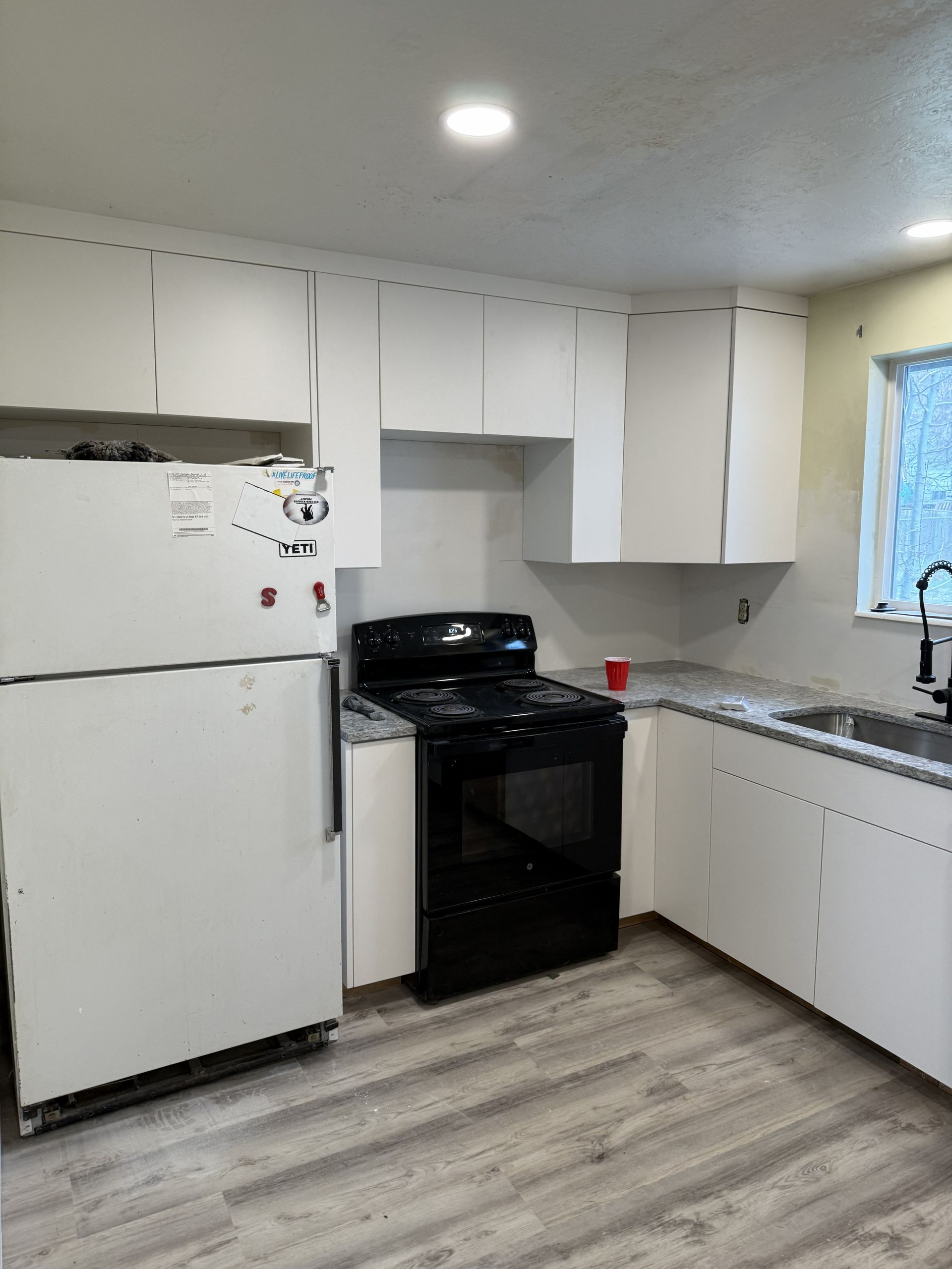 A kitchen with white cabinets, a black stove, a white refrigerator, and grey wood-look flooring.