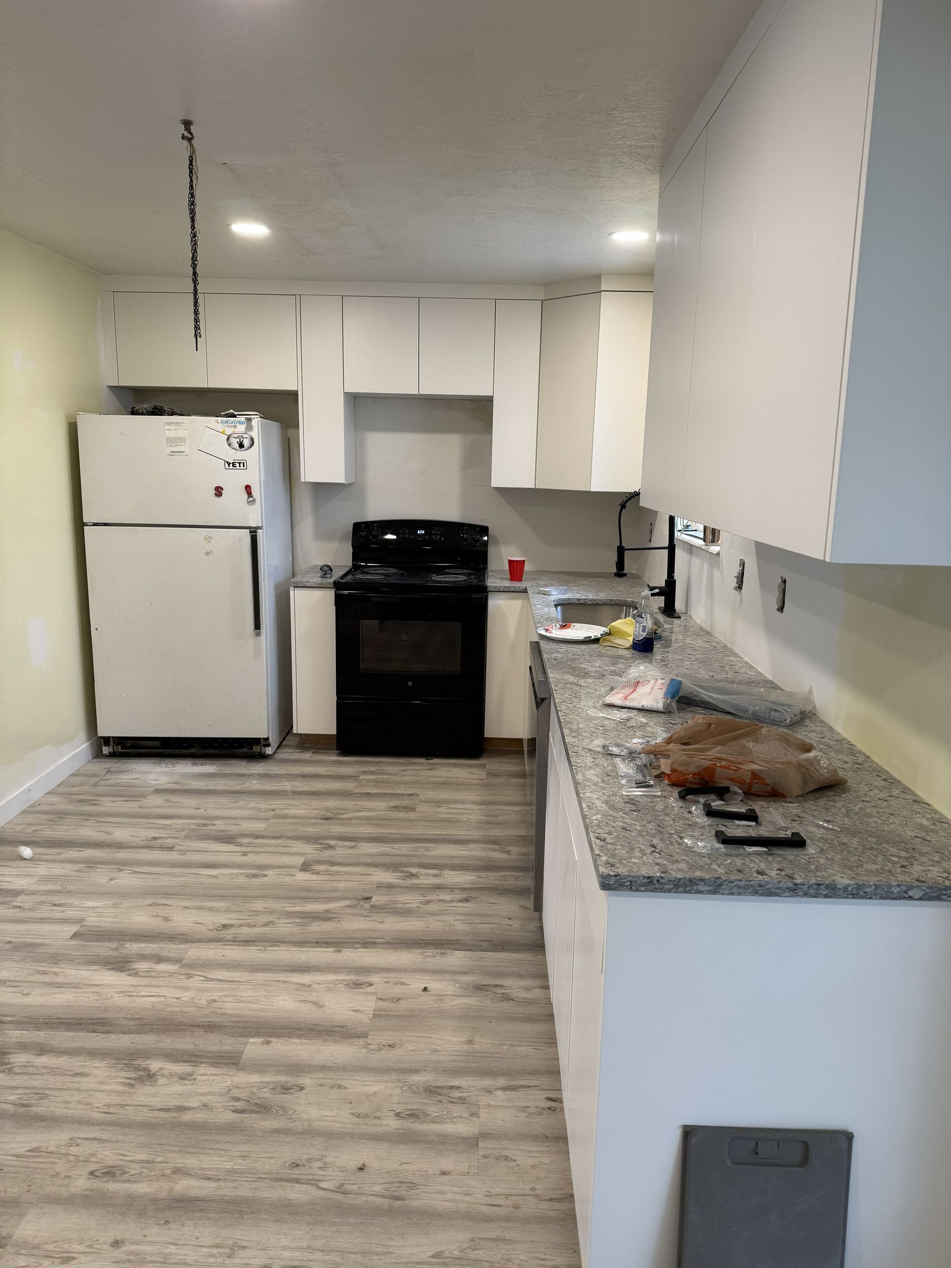 A kitchen with white cabinets, a black stove, a white refrigerator, granite-style countertops, and light wood flooring.
