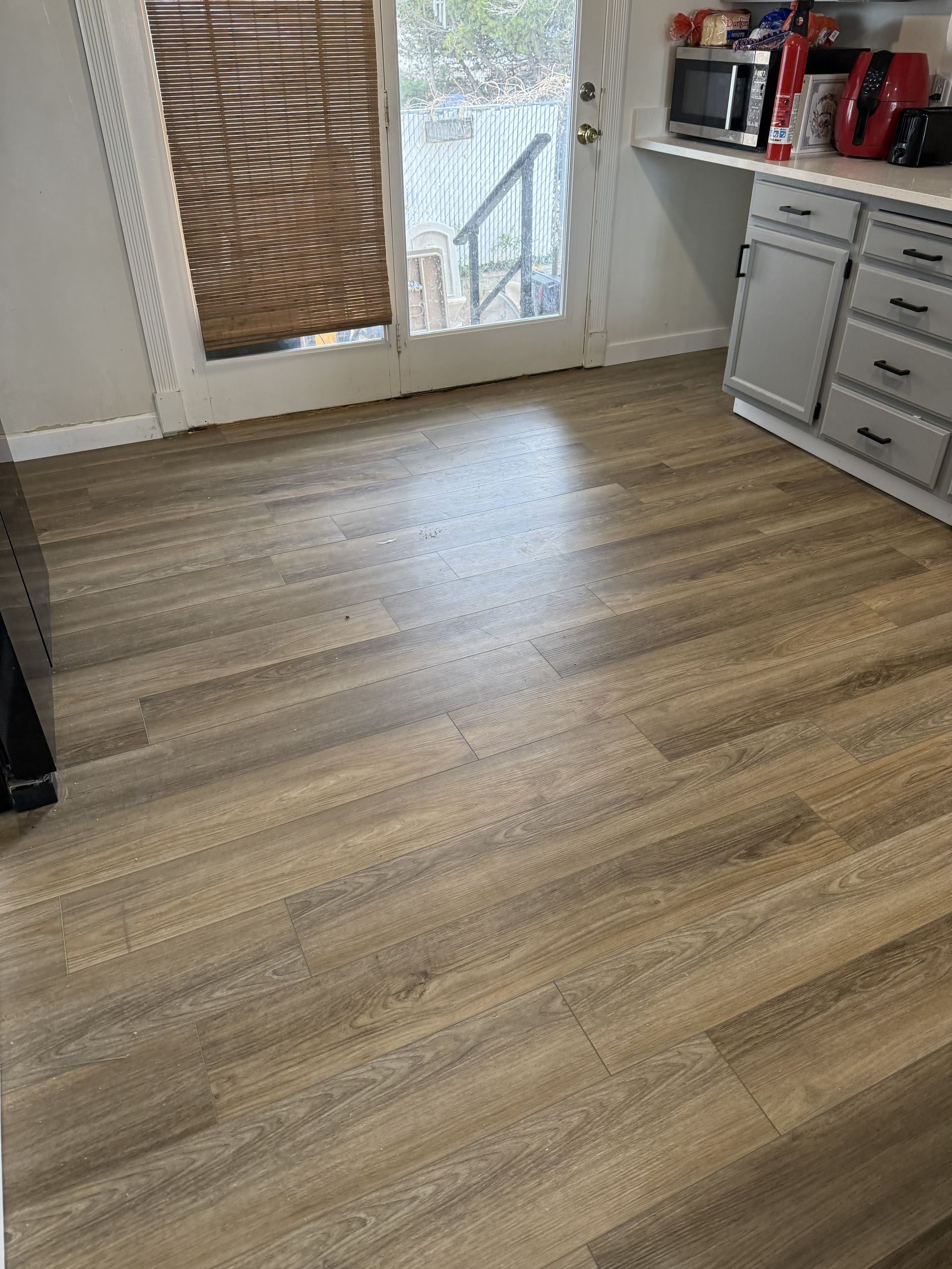 A wide shot of a kitchen with light-colored, wood-look plank flooring, a glass patio door, and gray cabinetry.