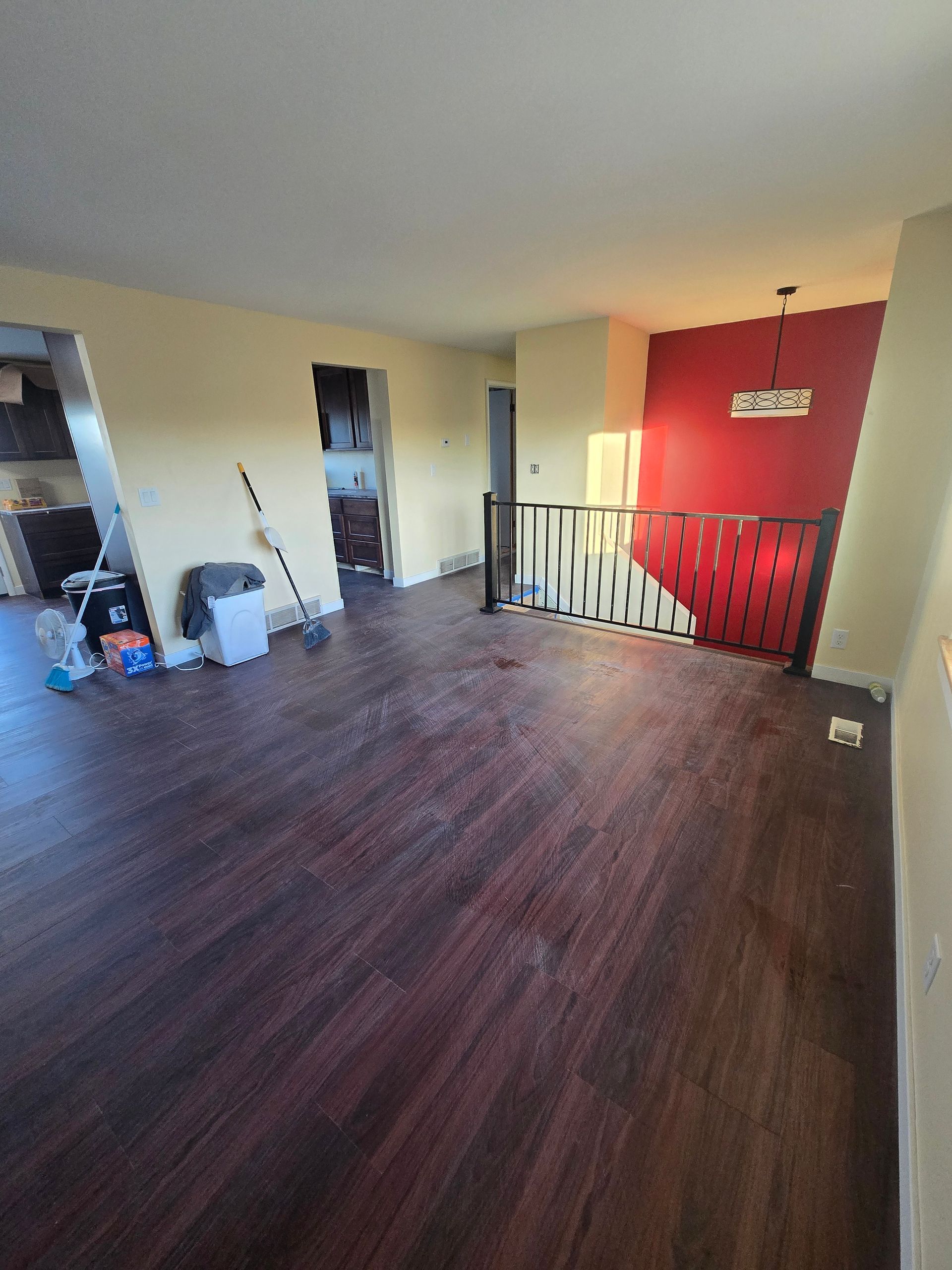 A living area with dark wood floors, yellow walls, and a staircase with a red accent wall and black metal railing.