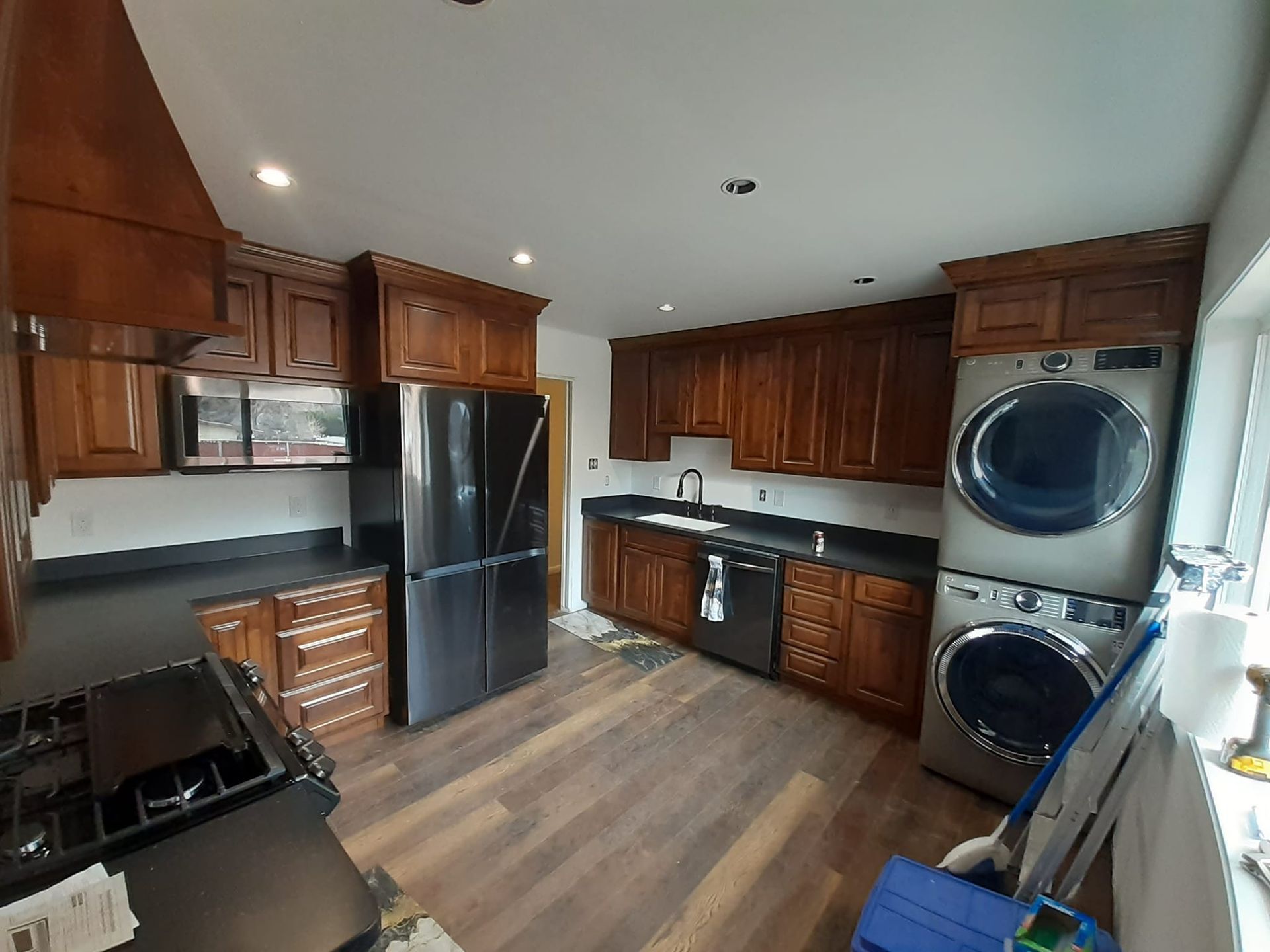 A modern kitchen with dark wood cabinets, black appliances, dark countertops, and a stacked washer-dryer unit.