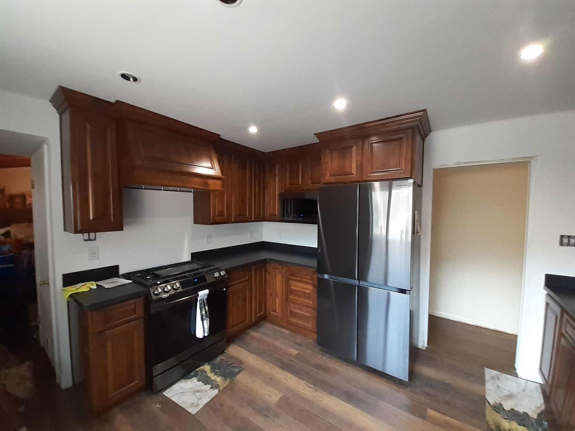 A modern kitchen featuring wood cabinets, dark countertops, a black oven range, and a stainless steel refrigerator.