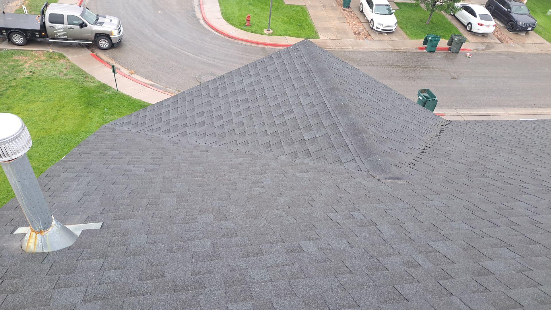 A high-angle view of a gray asphalt shingle roof on a residential home with a suburban street visible in the background.