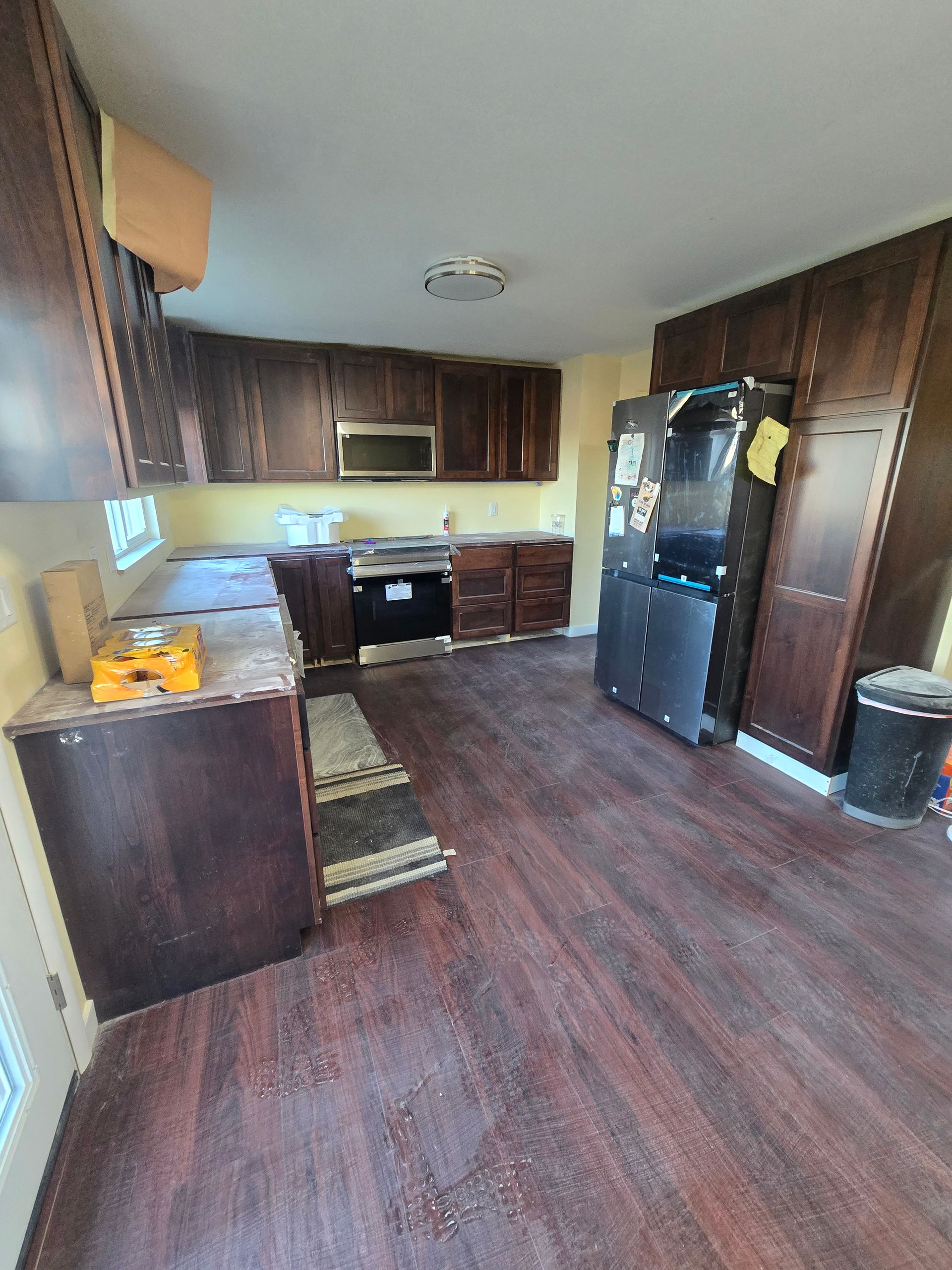 A kitchen under renovation with dark wood cabinets, a stainless steel oven, a black refrigerator, and wood-look flooring.
