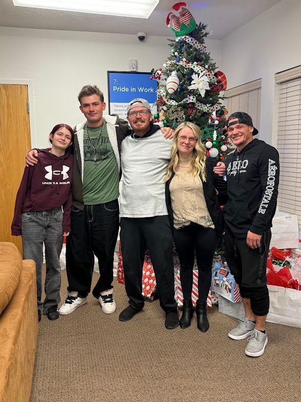 Five people posing beside a decorated Christmas tree and wrapped gifts.
