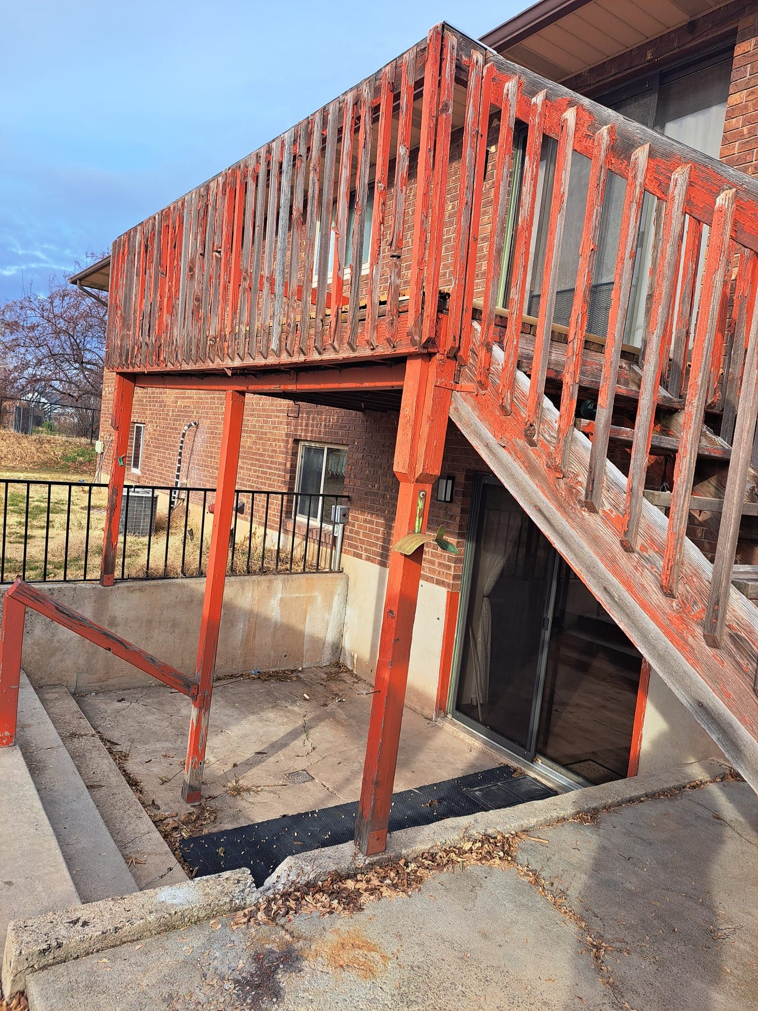 A red wooden staircase leads up to a deck above a basement entrance with a brick house exterior.