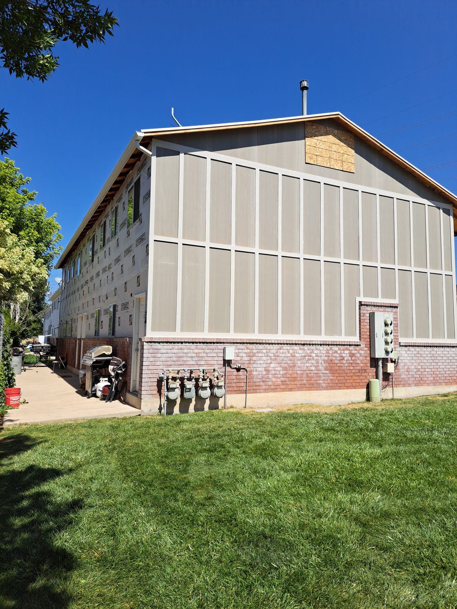 A multi-story building exterior under renovation with exposed sheathing over a brick base on a sunny day.