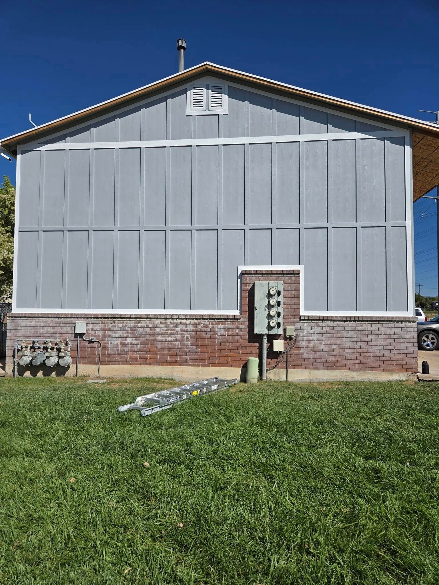 A side view of a house with light grey panel siding above a brick foundation, featuring an outdoor electrical box.