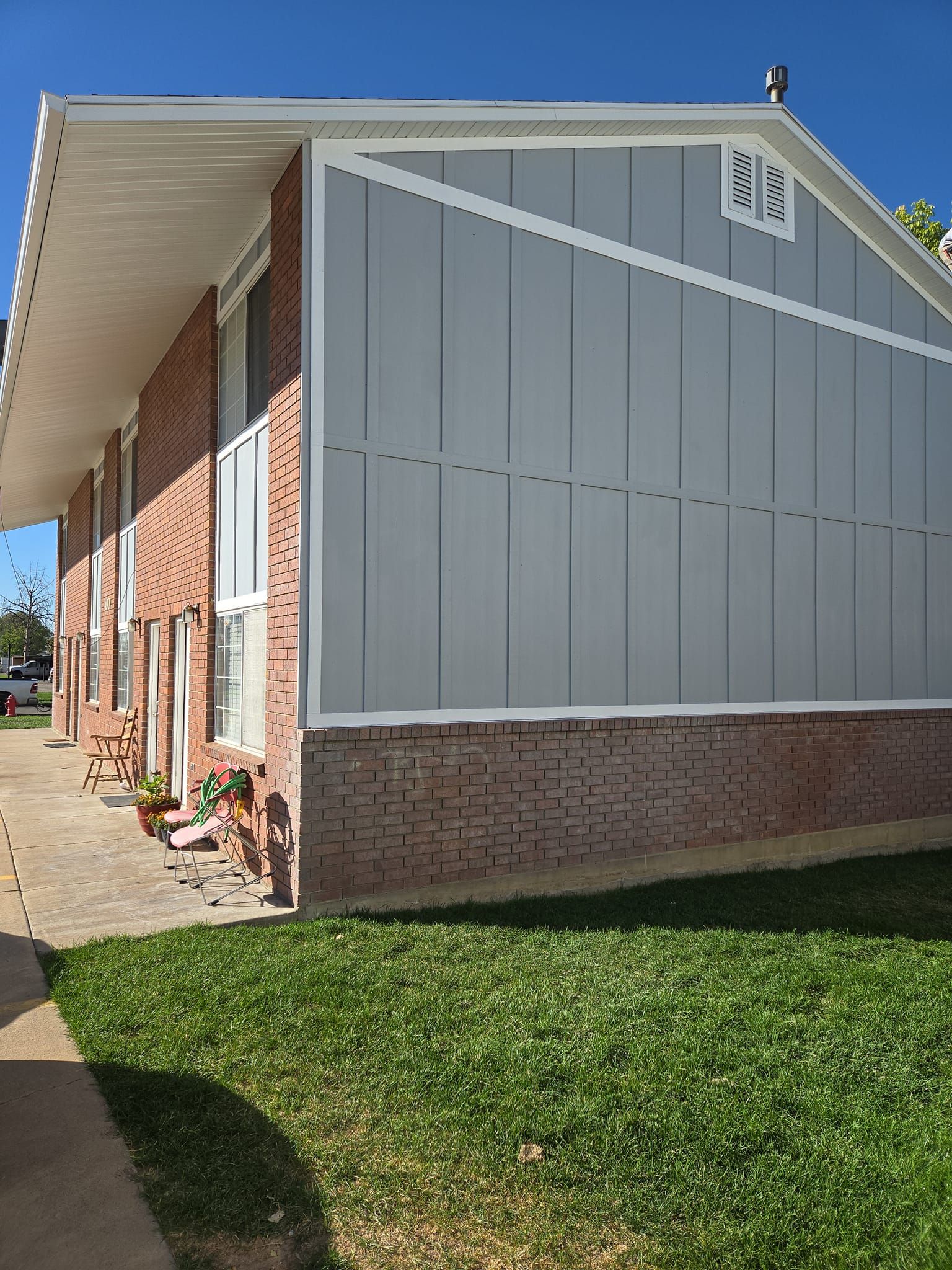 A side view of a residential building featuring a large gray paneled gable above a lower red brick wall and lawn.