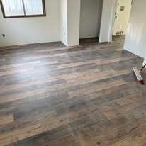A light-filled room with freshly installed brown and gray wood-look laminate flooring and a floor squeegee in the corner.