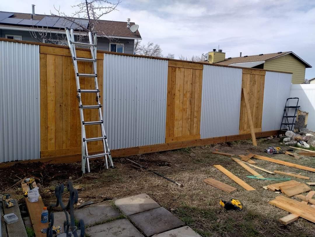 A newly constructed backyard fence with alternating vertical panels of wood and corrugated metal, with a ladder leaning.