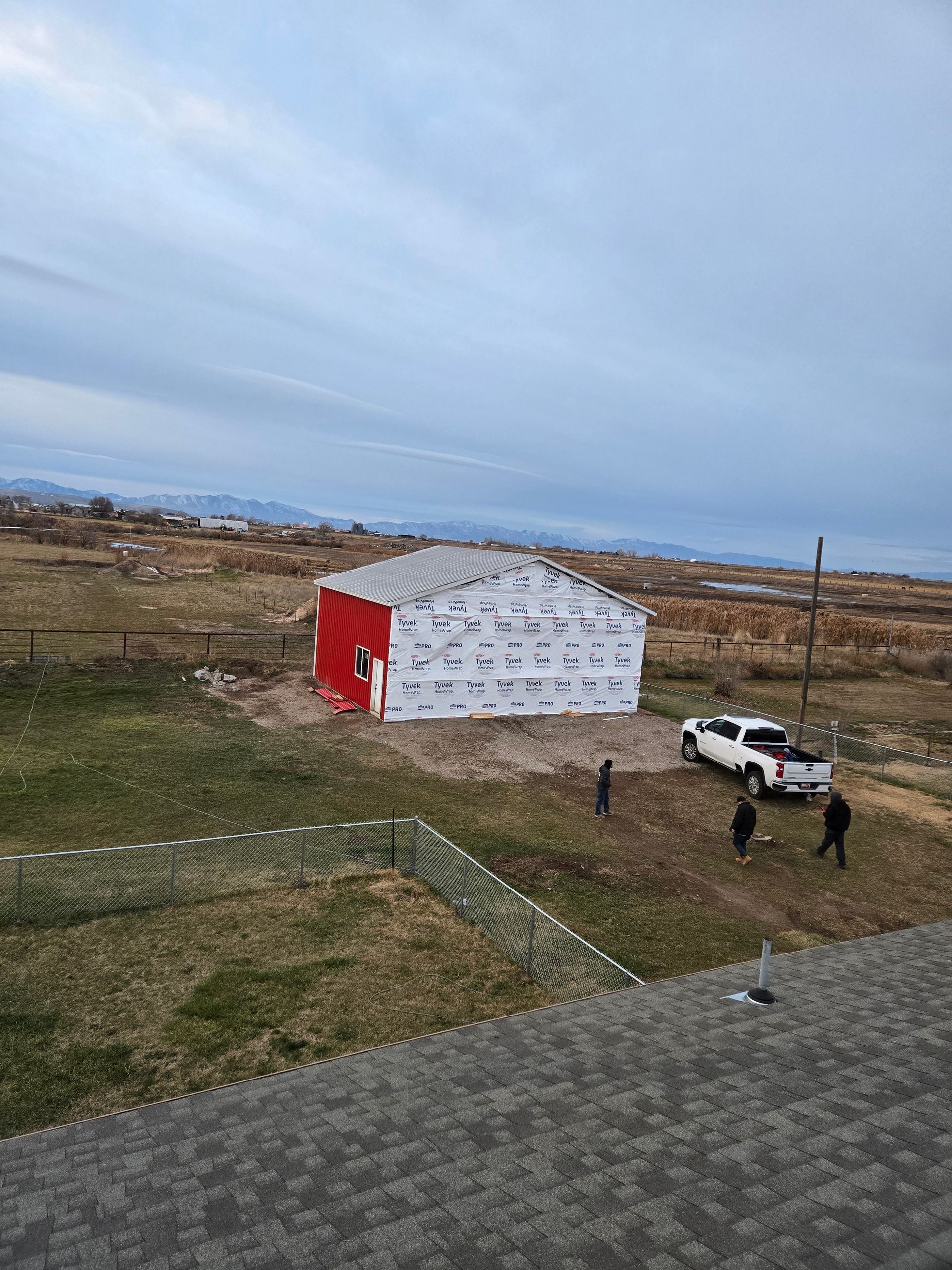 A white building under construction stands in a field next to a white pickup truck, with three people nearby.