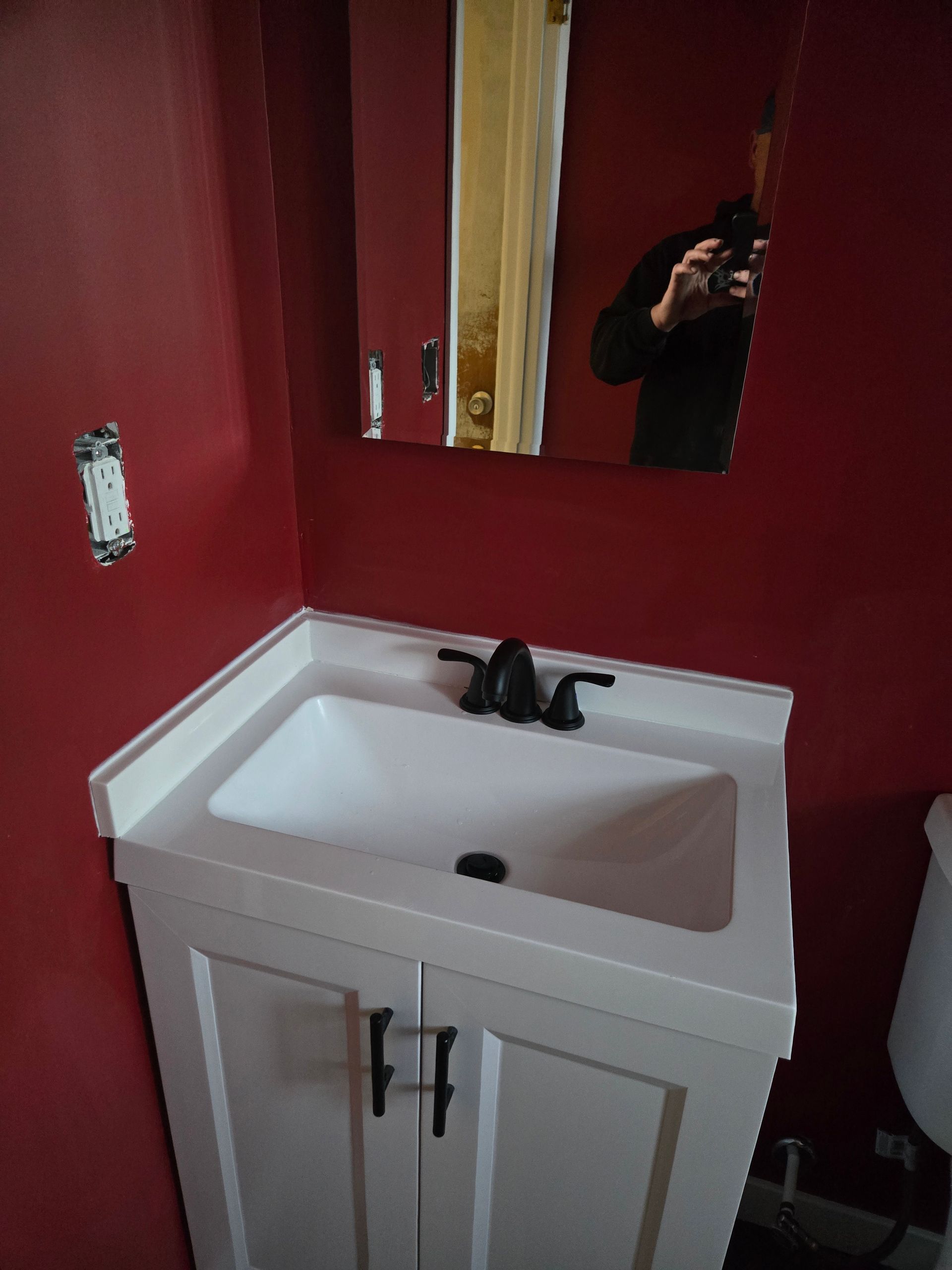 A white bathroom vanity with a black faucet sits against a deep red wall with a mirror above it.