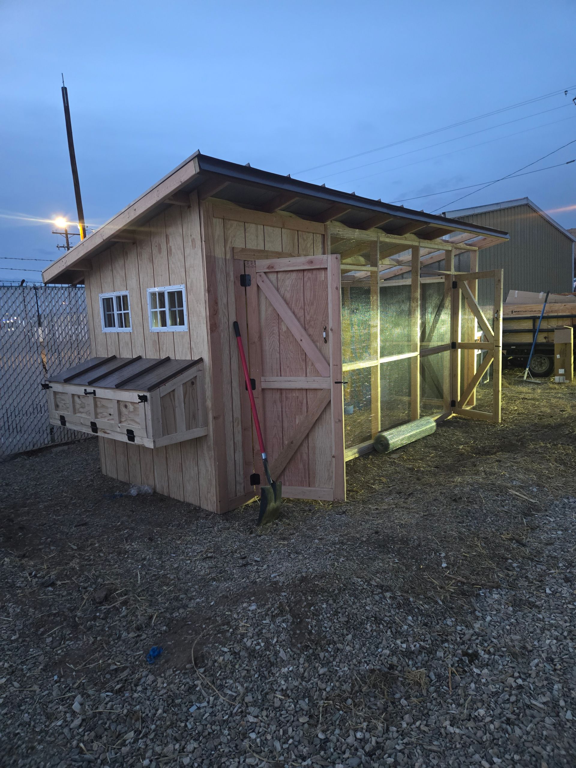 A newly built wooden chicken coop with an open door and attached nesting boxes, situated on gravel in a backyard.