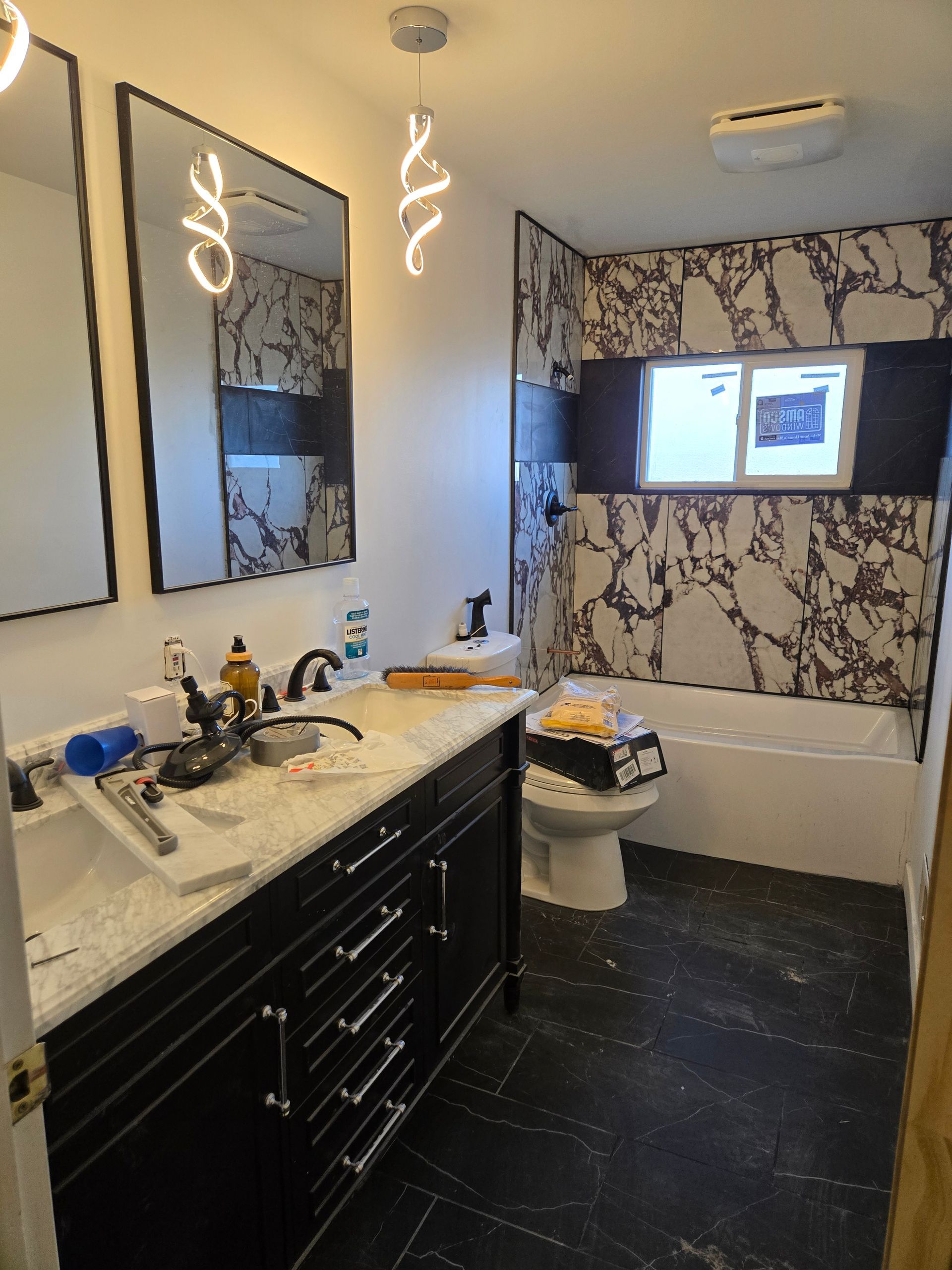A modern bathroom featuring a black vanity with marble countertop, dual mirrors, contemporary lights, and a marble shower.