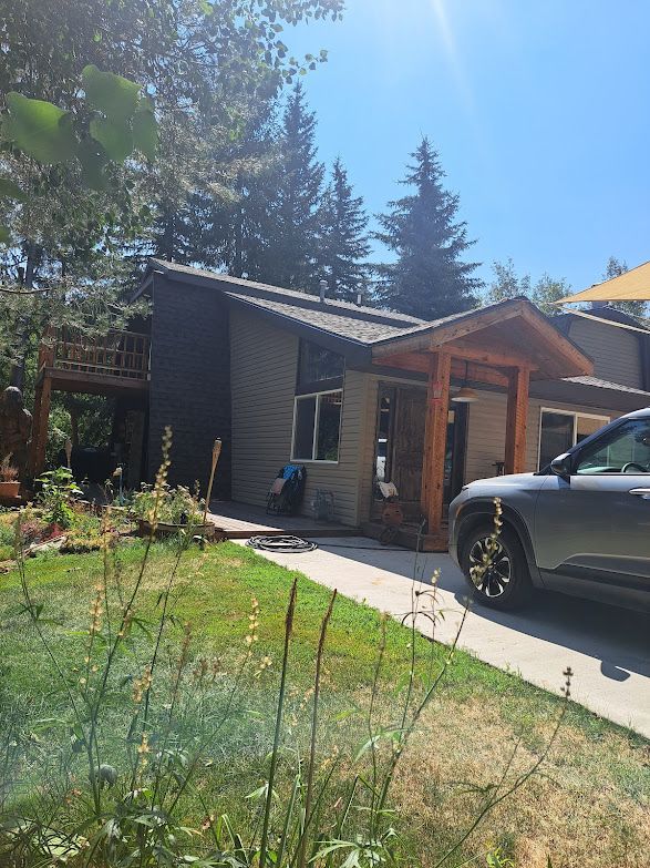 A gray house with a wooden porch and a vehicle parked in the driveway on a sunny day.