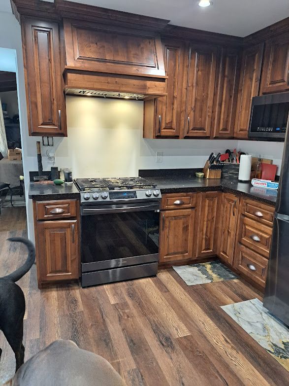A kitchen with dark wood cabinets, a stainless steel stove, and wood-patterned flooring.