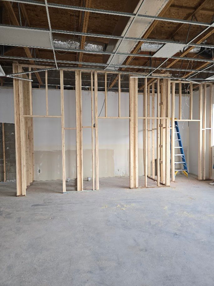 Interior view of a room under construction featuring newly framed wooden stud walls and a ceiling grid.