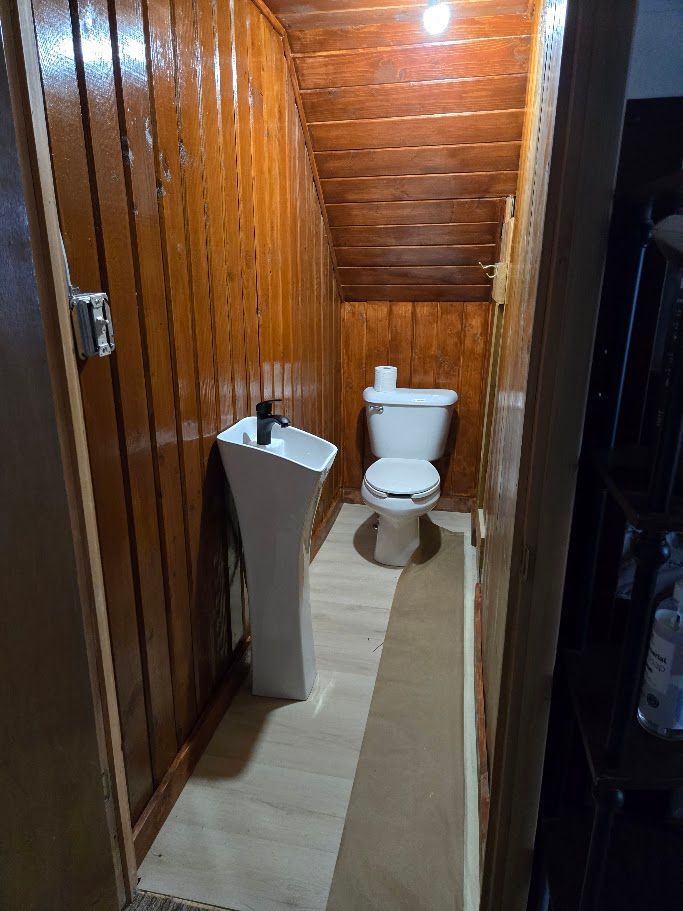 A narrow bathroom with wood-paneled walls and ceiling, featuring a white pedestal sink and a toilet.