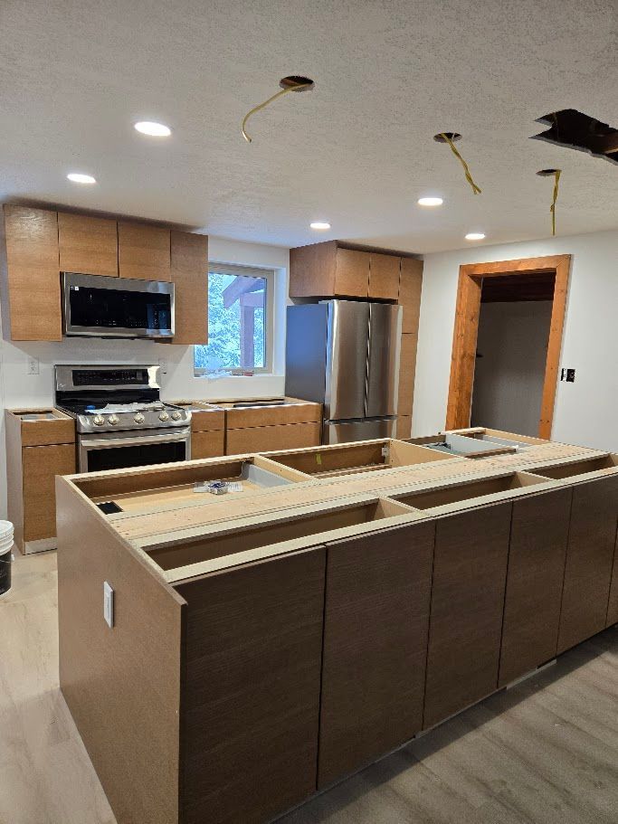 A kitchen under construction featuring wooden cabinets, a stainless steel refrigerator, and an island without a countertop.