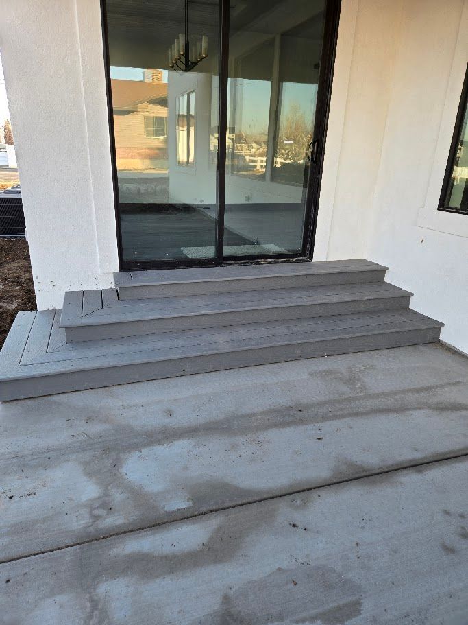 Two grey wooden steps leading up to a glass sliding door on a concrete patio.
